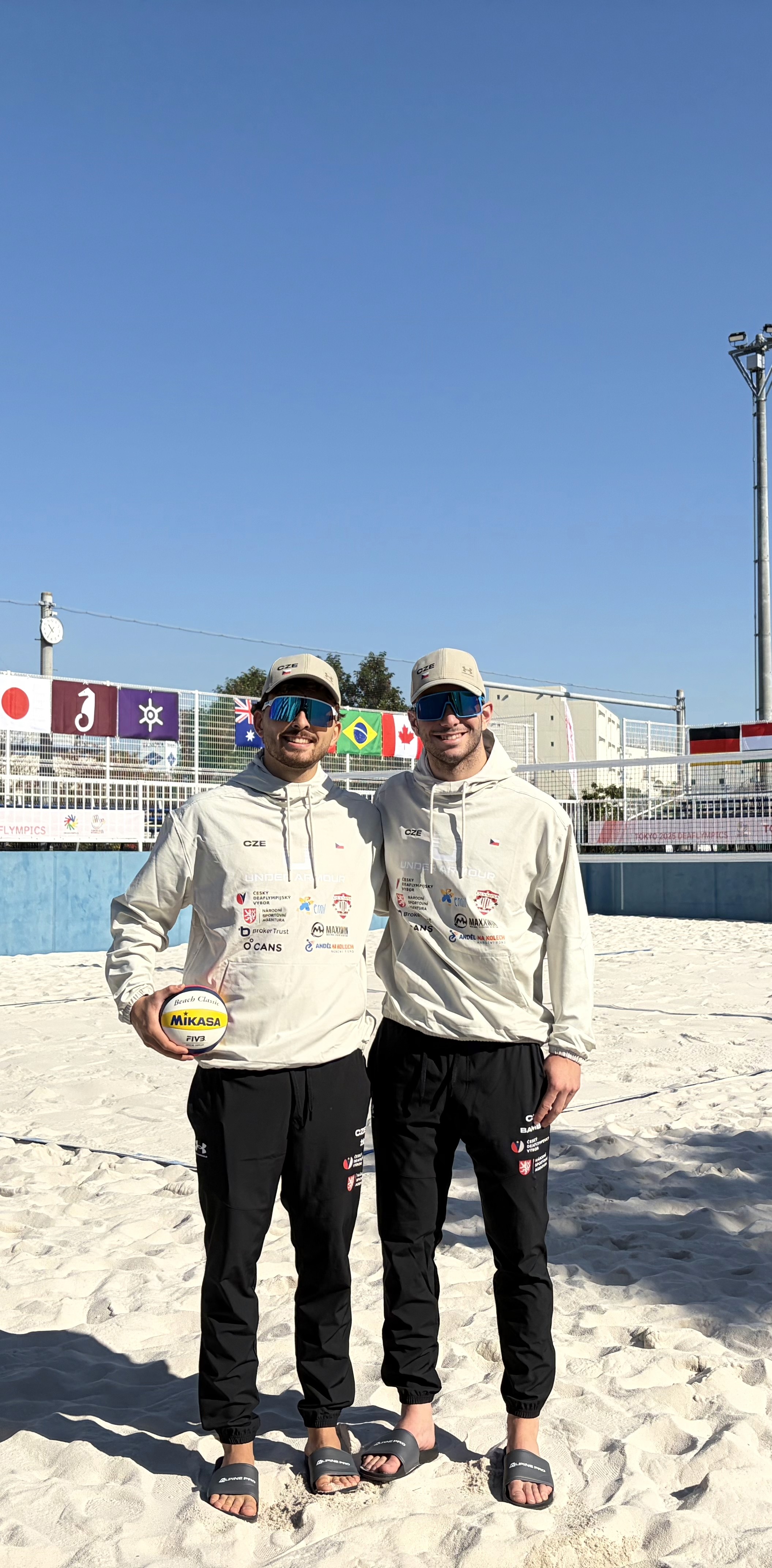 Jan Žídek a Šimon Bambas na beachvolejbalovém kurtu v Tokiu v reprezentační teplákové soupravě.