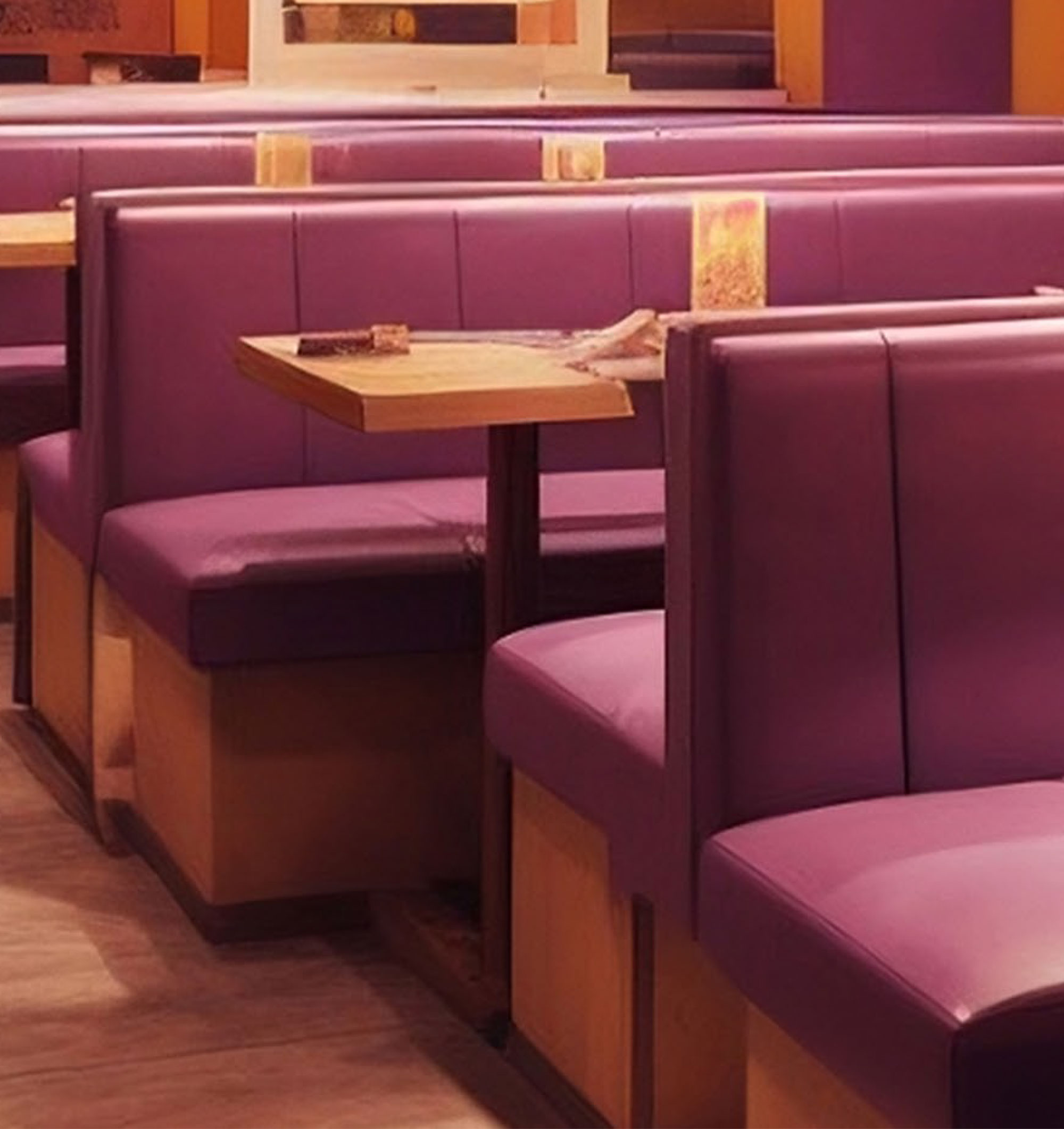 Interior of a restaurant featuring purple upholstered booths and wooden tables, arranged for dining.