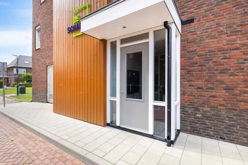 De geopende voordeur van het appartementencomplex onder een witte luifel.