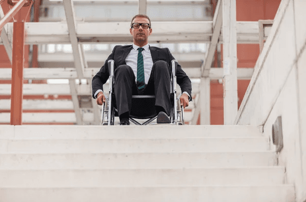 homem de terno e cadeirante no degrau mais acima de uma escada, olhando para baixo