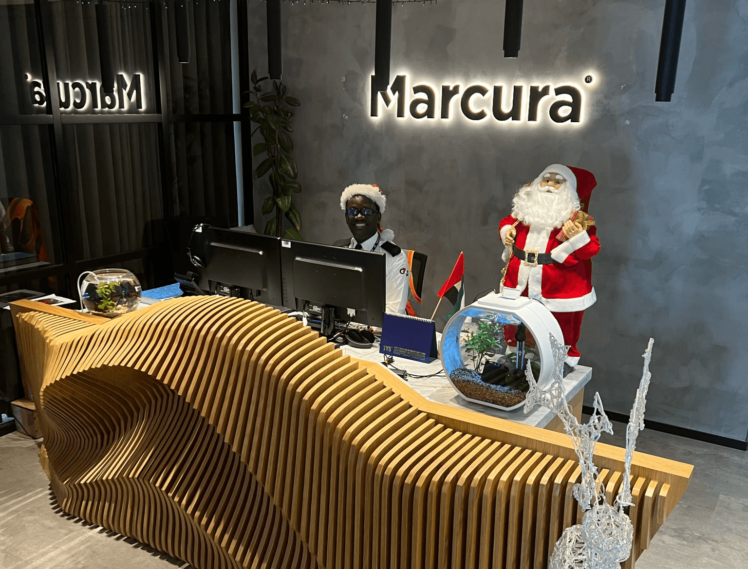 A festive scene featuring a character in a Santa costume at a modern reception desk with decorative elements.