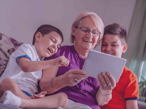 Grandmother and her two grandchildren smiling while using Glimpse on a tablet to connect with a deceased loved one.