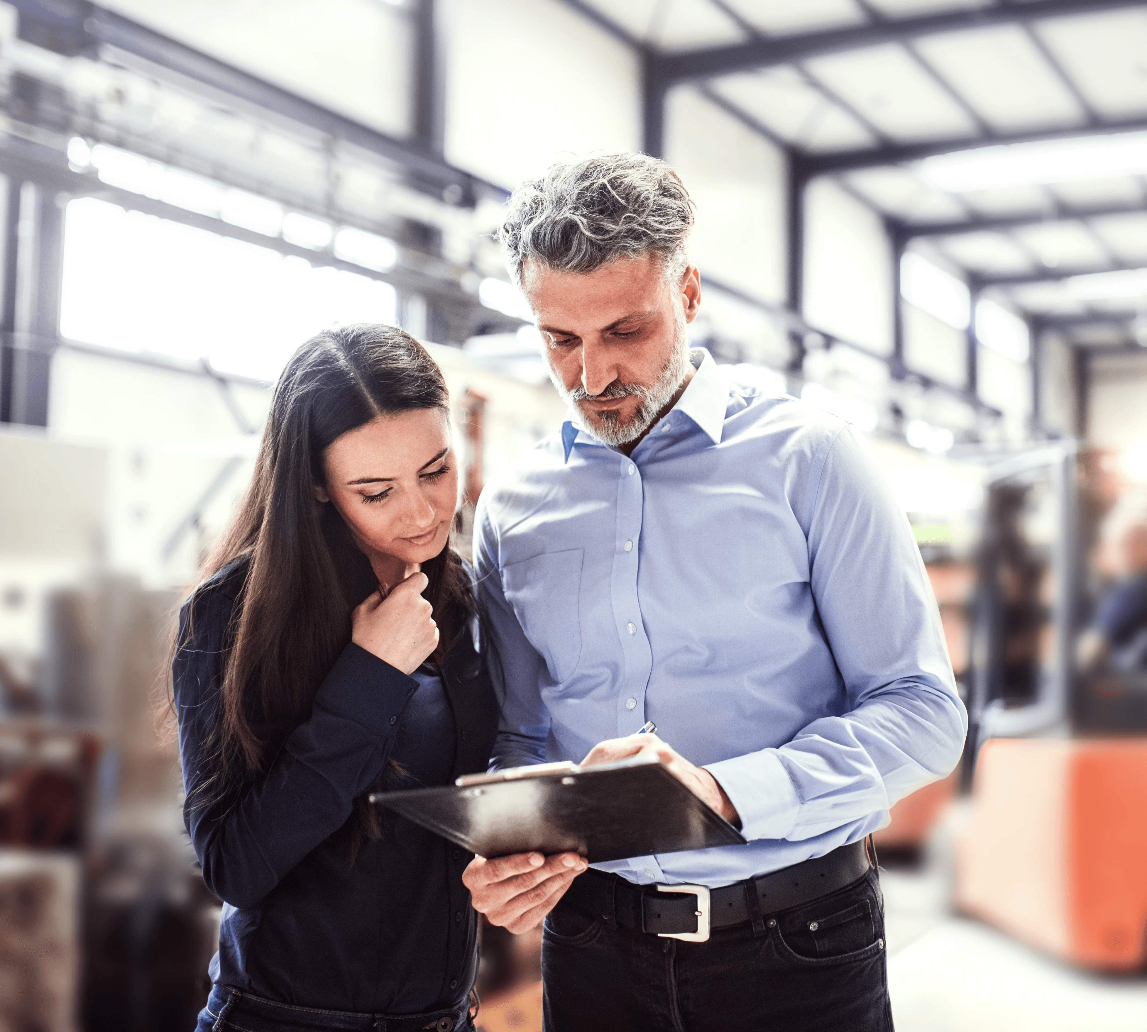 Zwei Mitarbeitende in einer Lagerhalle schauen gemeinsam auf ein Klemmbrett und besprechen Notizen.