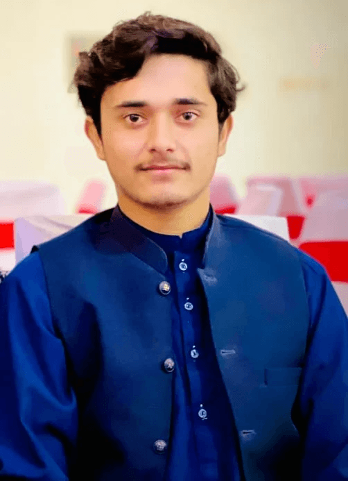 A young man with short, dark hair stands against a softly blurred background, wearing a traditional deep blue kurta with buttons and a matching waistcoat.