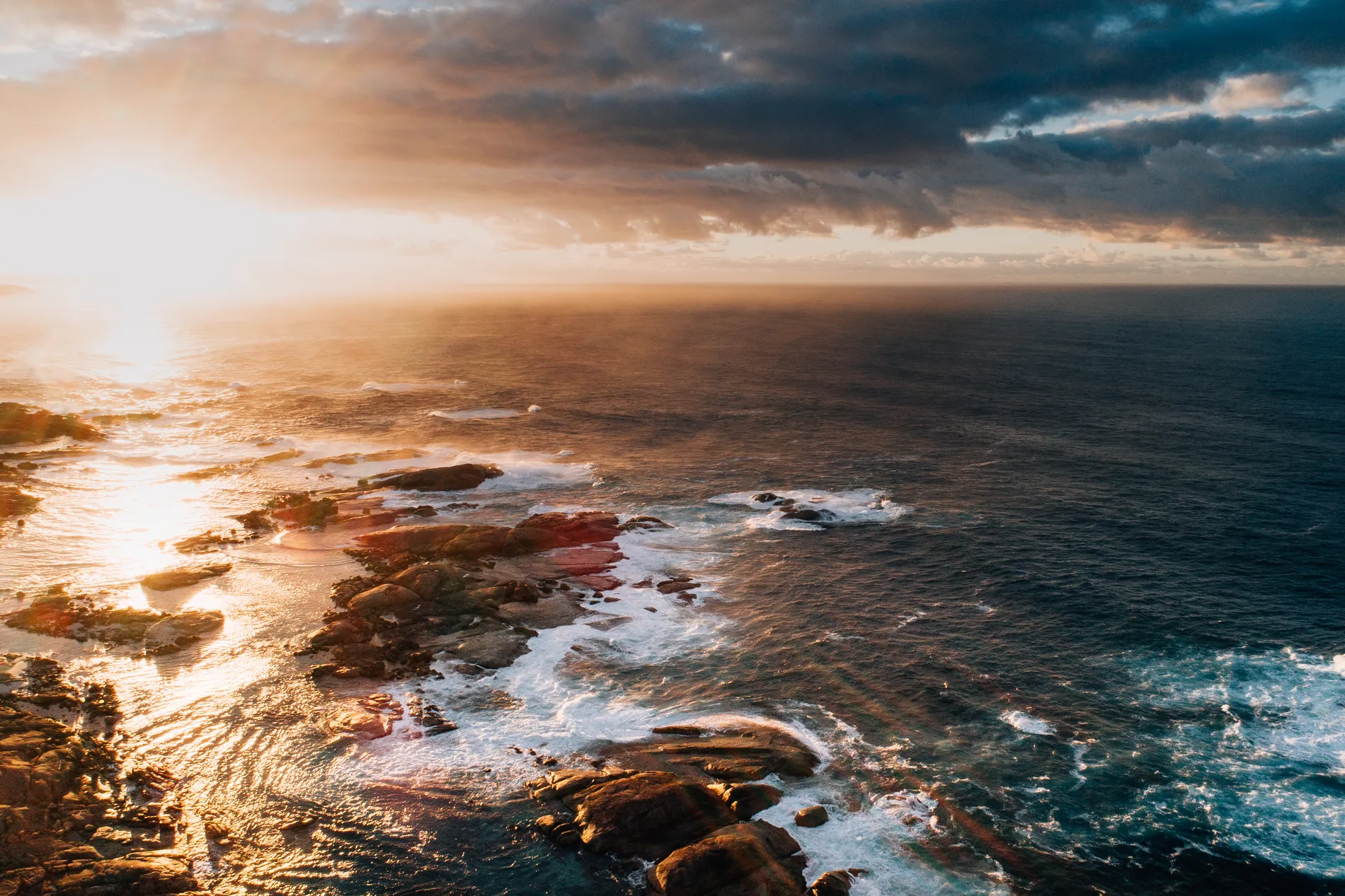 Sunset light breaking over a dark rocky coastline and heavy surf