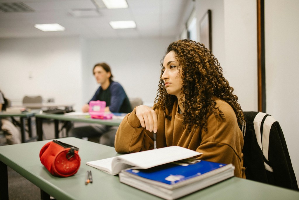 A concerned international student sitting at a desk in a Canadian college classroom, focused on maintaining her DLI enrollment and IRCC study permit compliance.