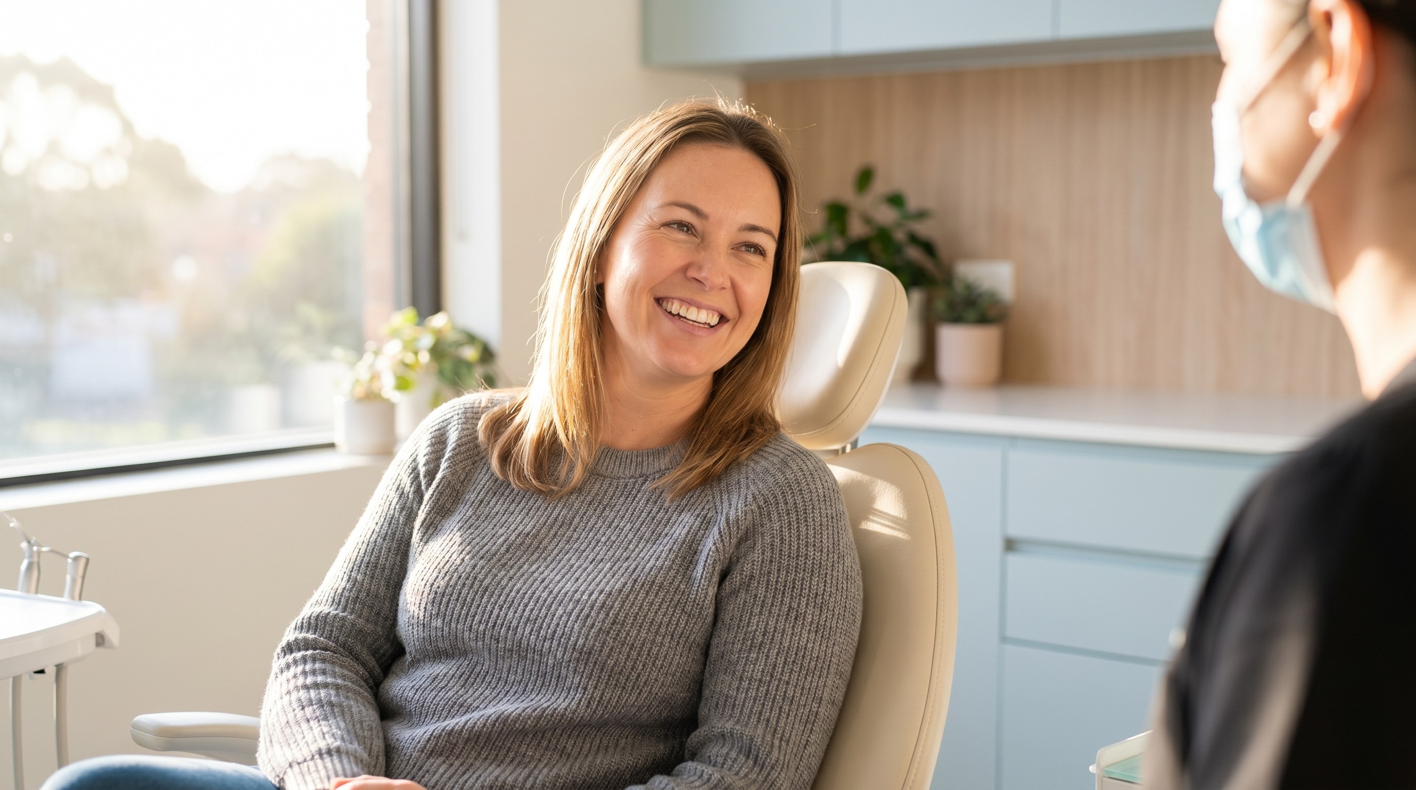 Adult woman smiling in a dental chair during a routine cleaning appointment with daylight from a window