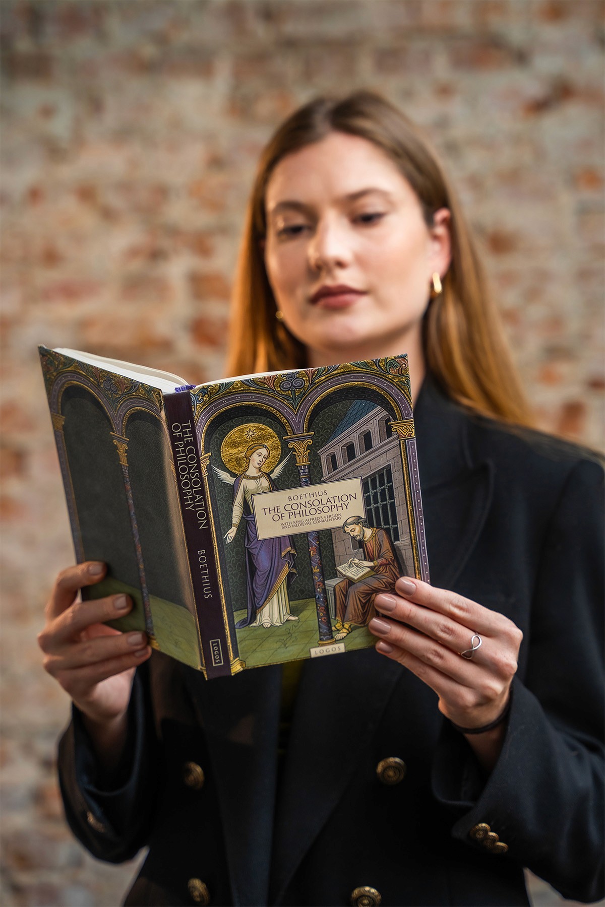 Woman wearing a black blazer holding the hardcover book The Consolation of Philosophy by Boethius, Logos edition.