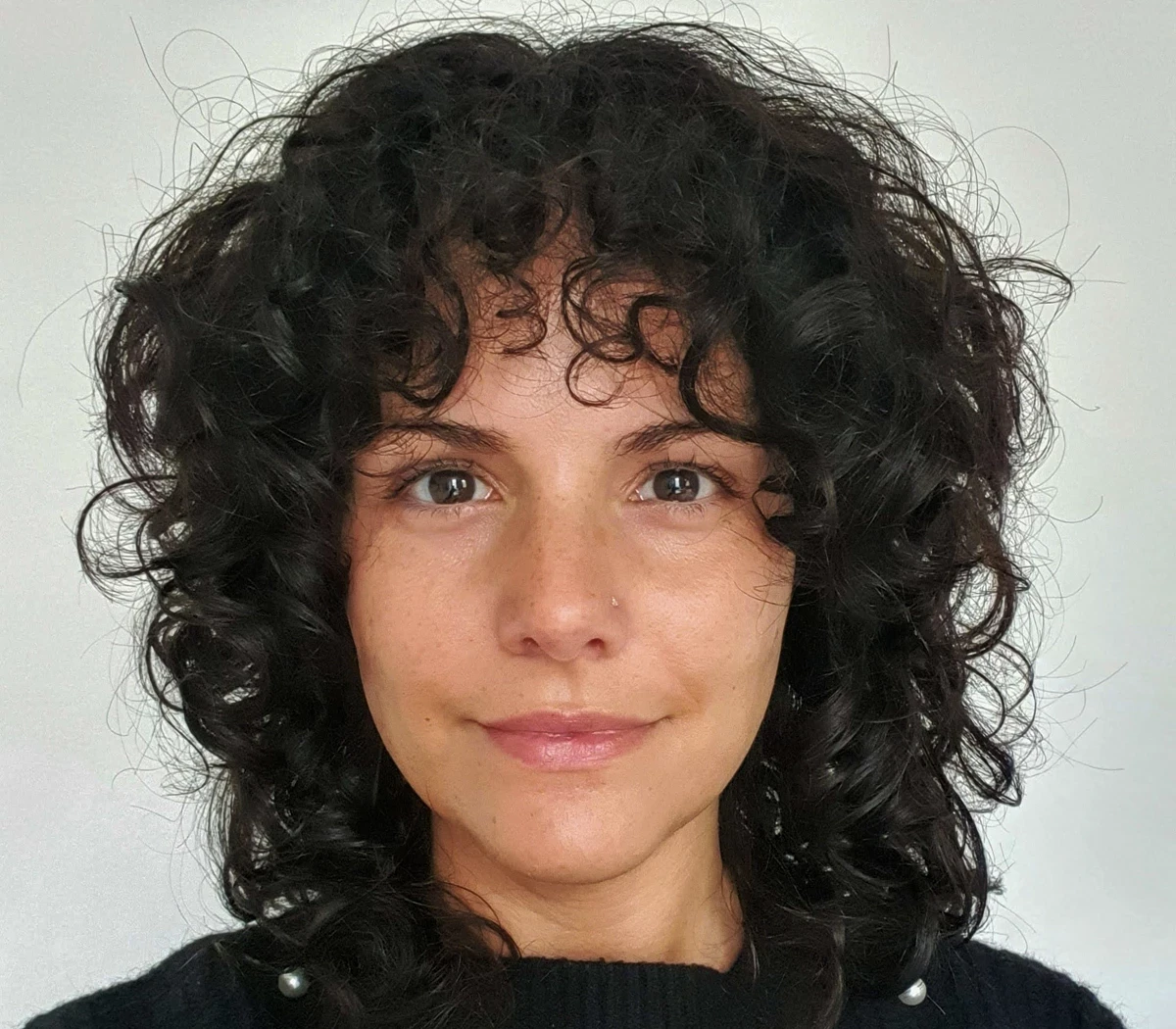 A woman with dark curly hair smiles at the camera against a white background