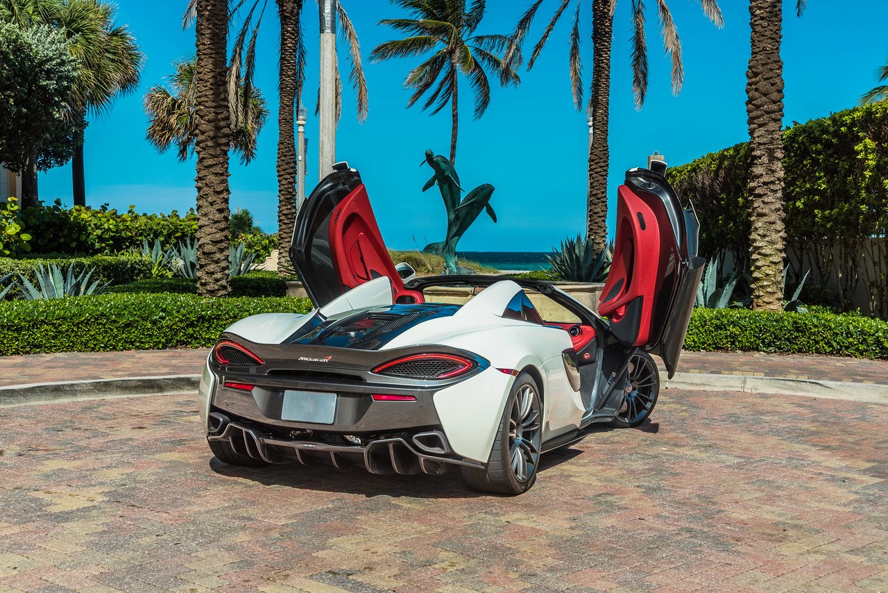 Side-angle shot of the McLaren 570S with both doors open, showcasing its sleek aerodynamic design and luxurious red interior.