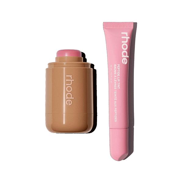 Smiling man in a grey blazer and graphic tee, lit by window shadows on a beige wall