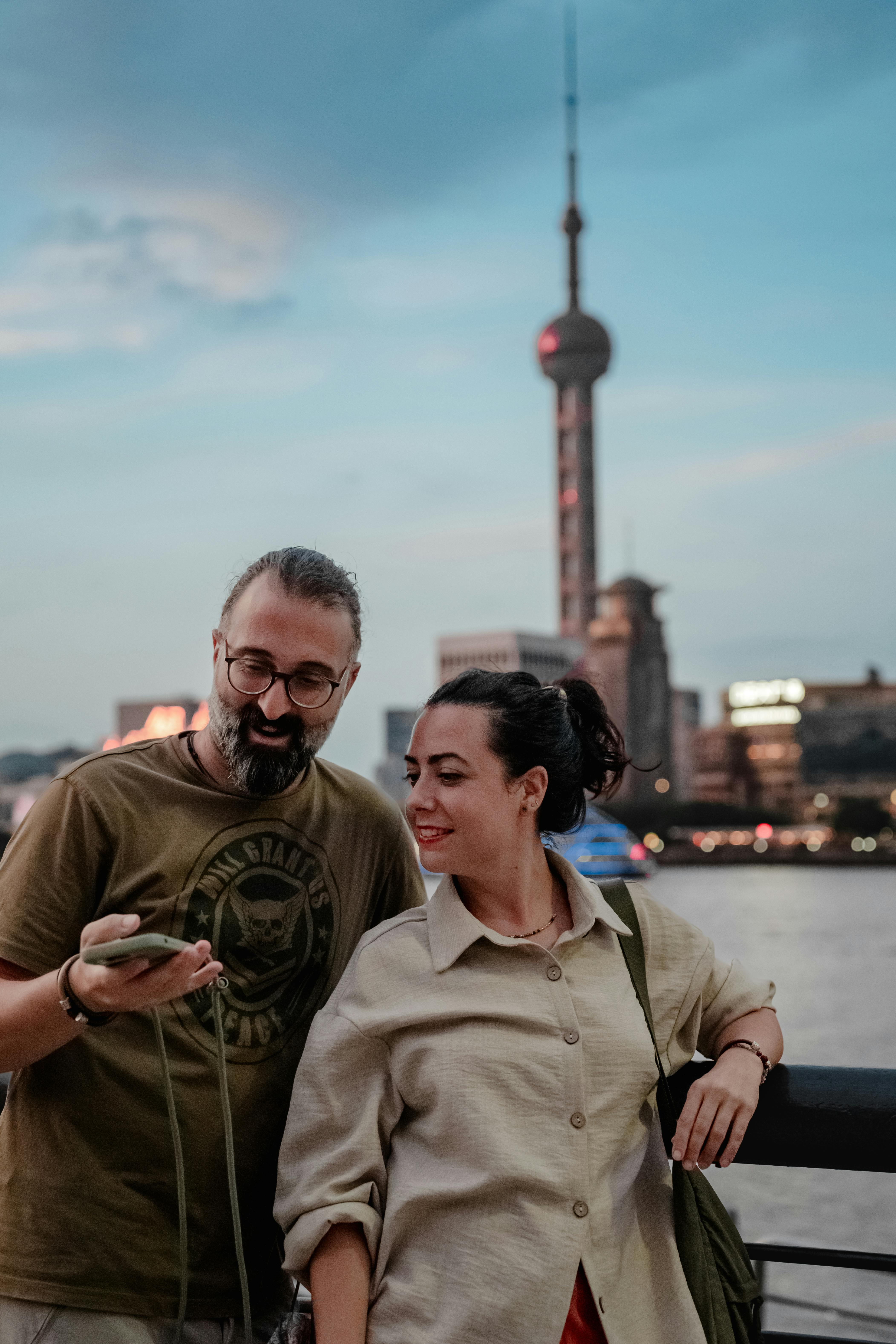 Two tourists by Shanghai's Huangpu River, Oriental Pearl Tower in background