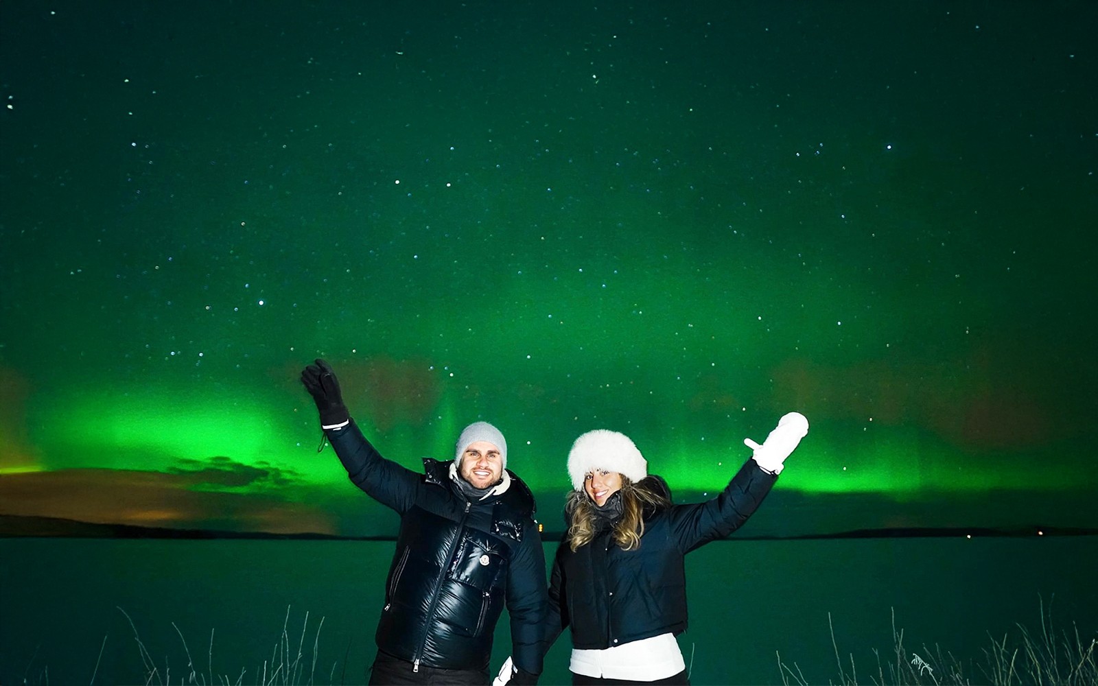 Northern Lights over snowy landscape with two people on Tromso Northern Lights Chase Tour.