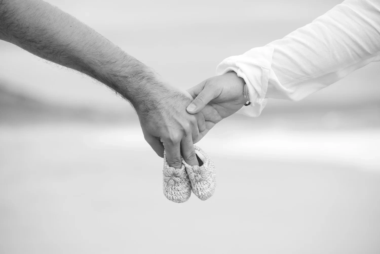 Close-up of two hands holding baby shoes in black and white