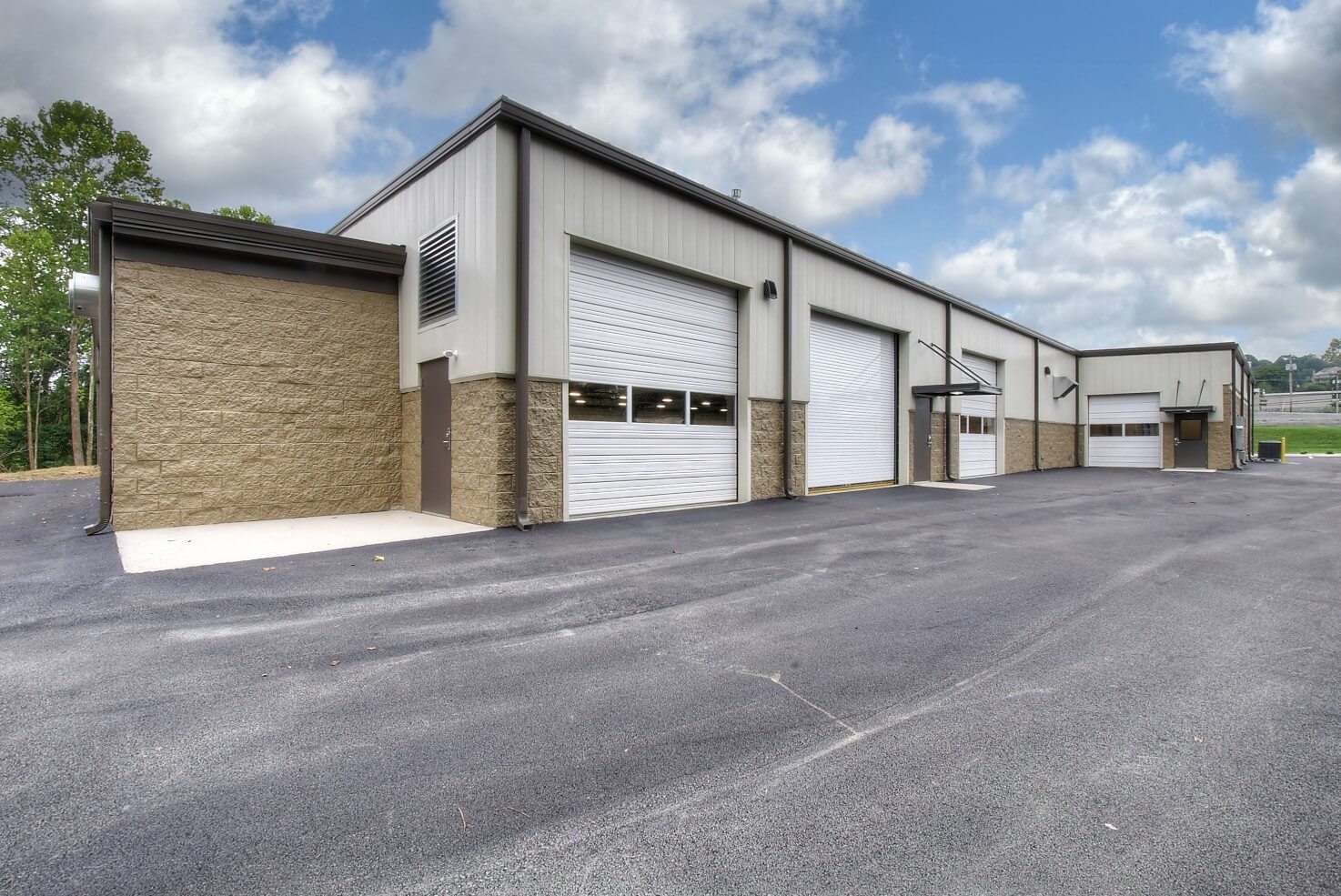 A modern commercial building with large doors, positioned on a paved lot under a partly cloudy sky.