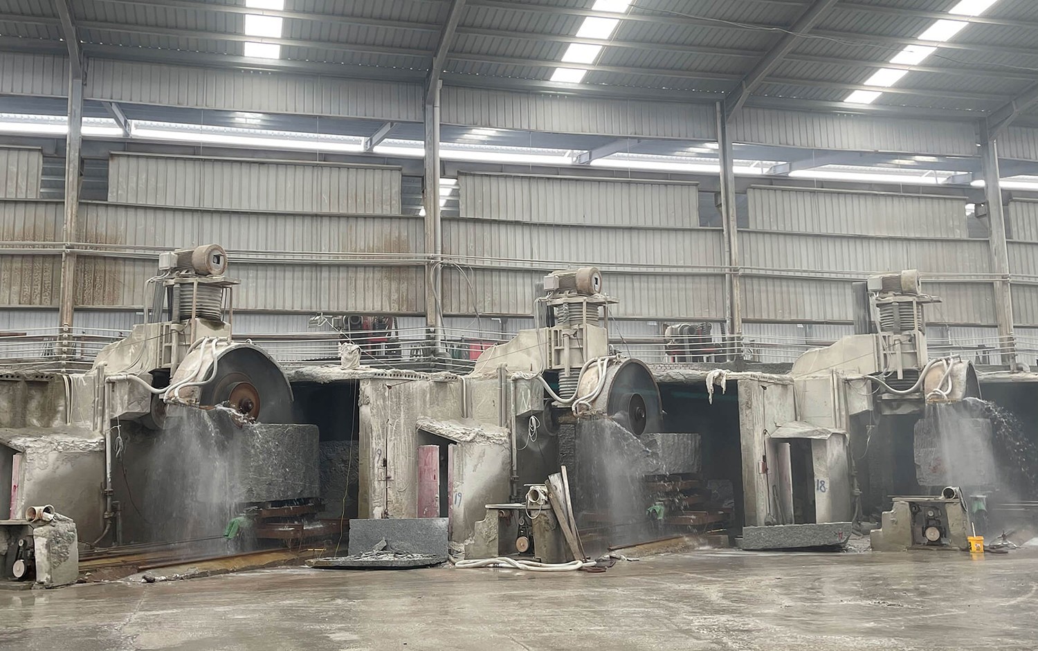 A row of Dinosaw Single Column Auto Cutting Machines in a production facility, each equipped with large cutting blades, actively cutting stone blocks with precision.