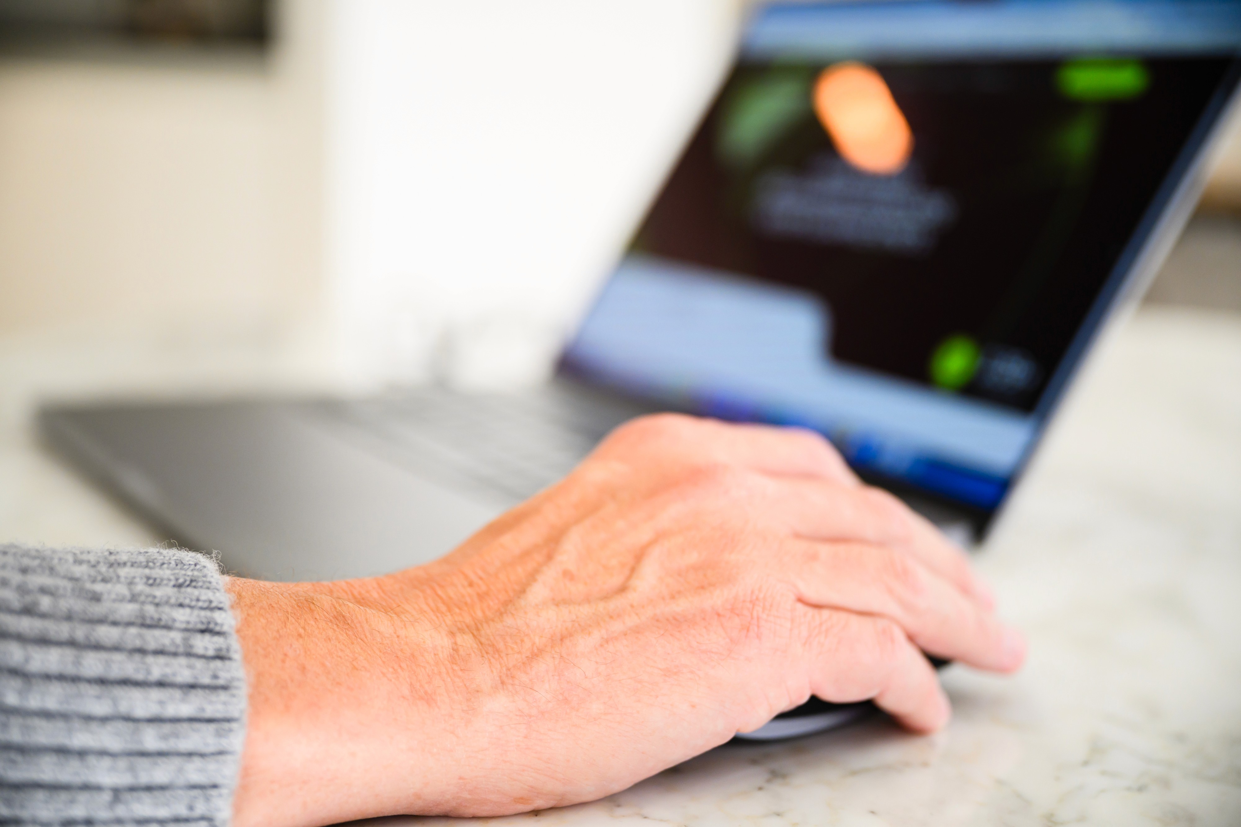 de hand van Hans op de muis met acheraan onscherp beeld van openstaande laptop