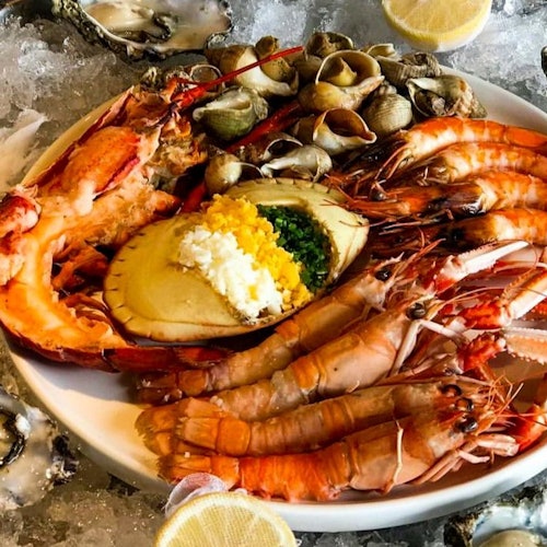 Platou cu fructe de mare asortate, inclusiv creveți, homar, scoici și o scoică Saint-Jacques cu garnitură, înconjurat de gheață și jumătăți de lămâie.
