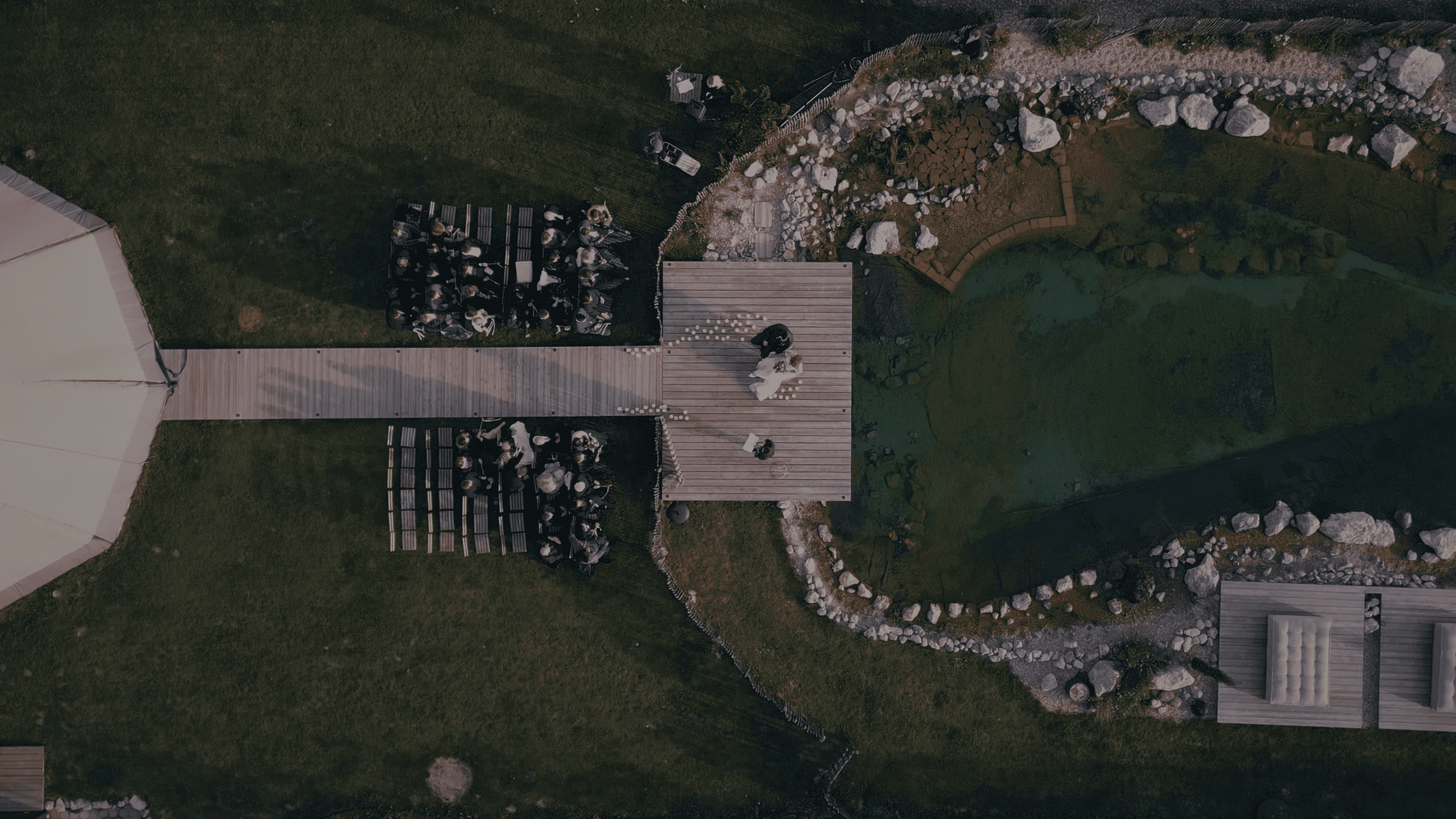 Aerial view of an outdoor destination wedding ceremony set beside water, captured from above