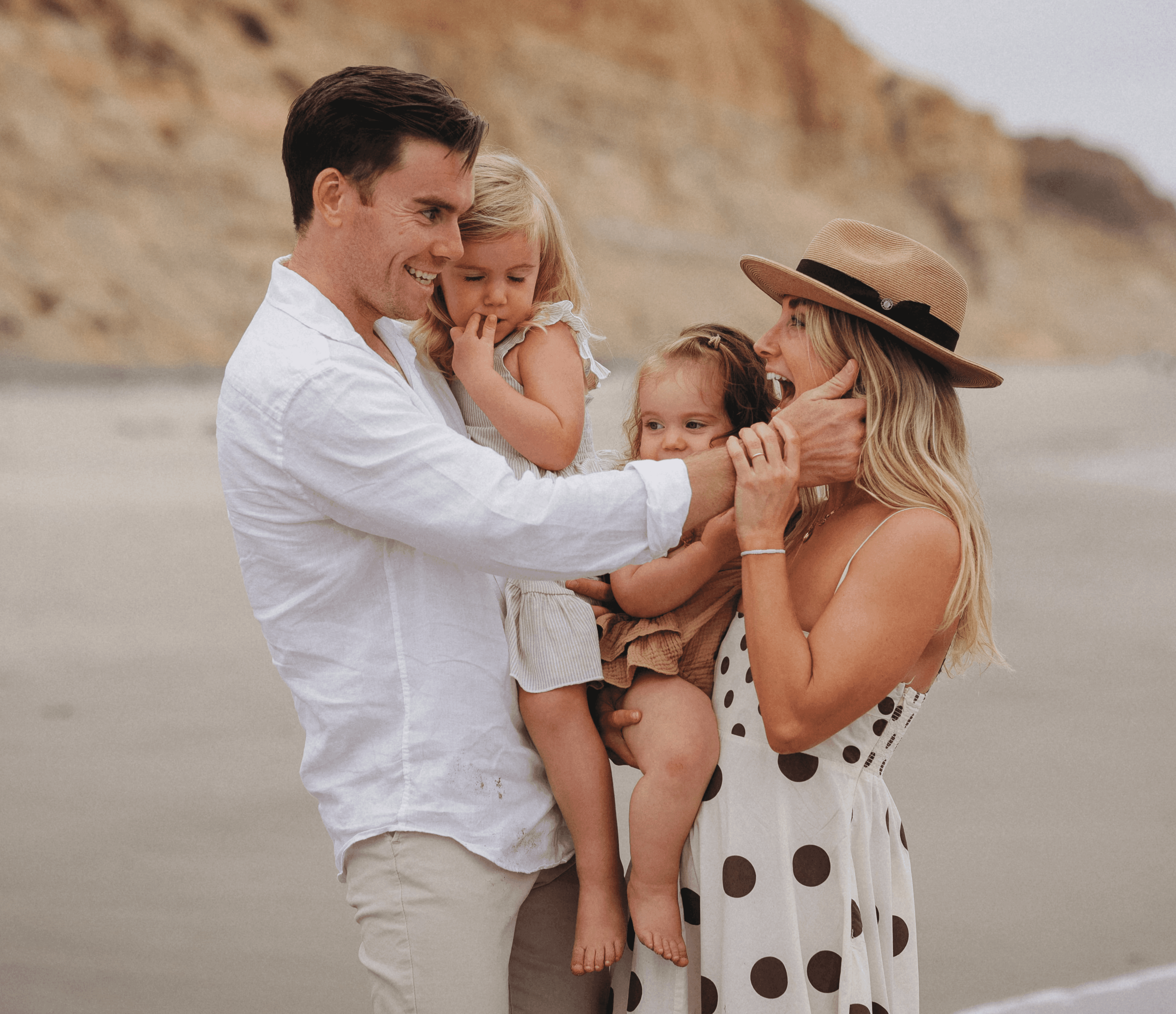 Family hugging and laughing together by the cliffs during a relaxed beach photoshoot in San Diego.
