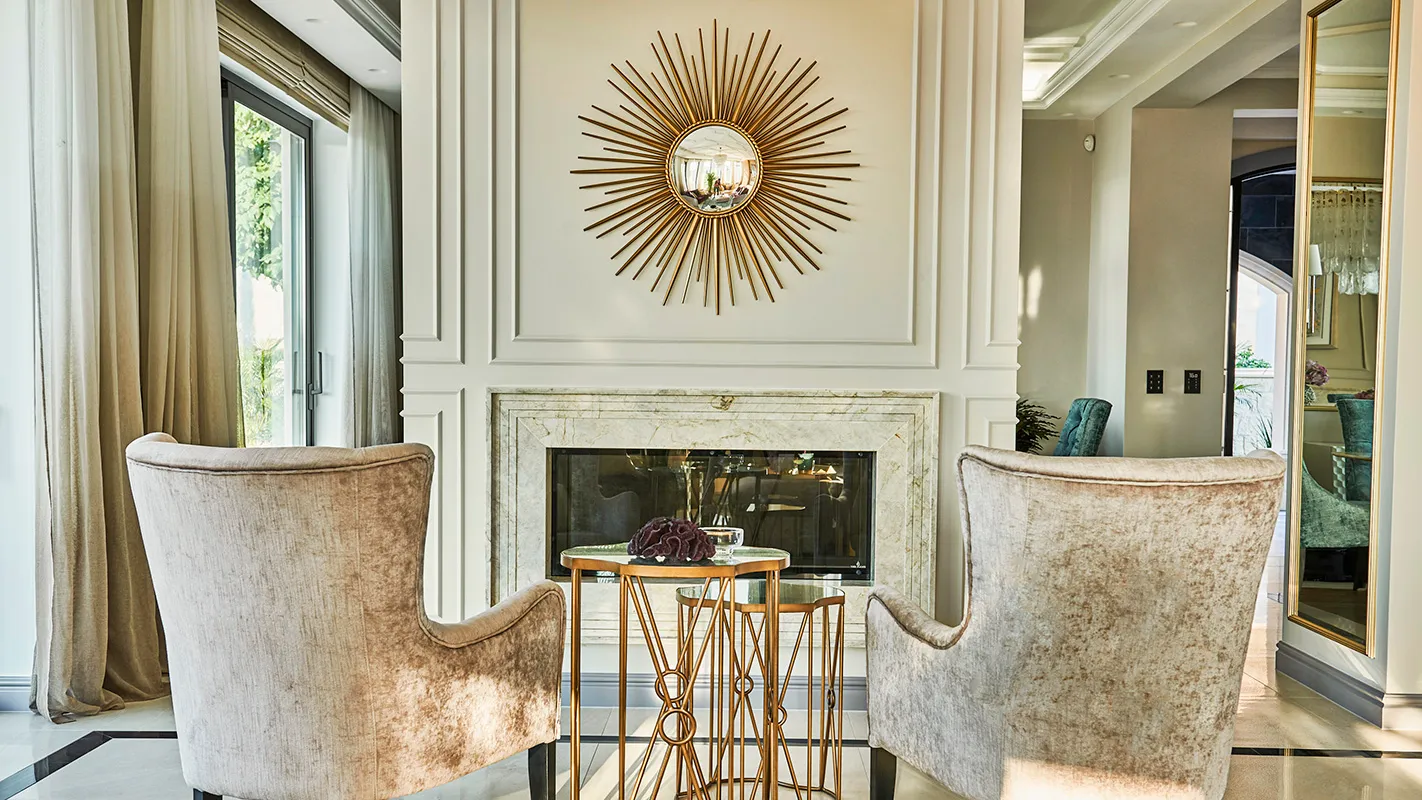 Villa Belmare lounge nook with marble fireplace, sunburst mirror, and plush armchairs