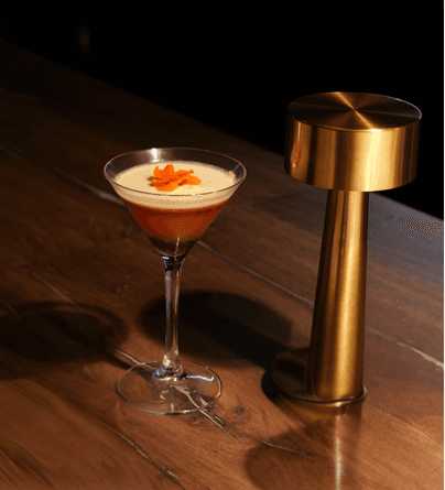 White plate with roasted carrots served on green sauce, topped with almonds and fresh herbs, held by a hand over a dark table.