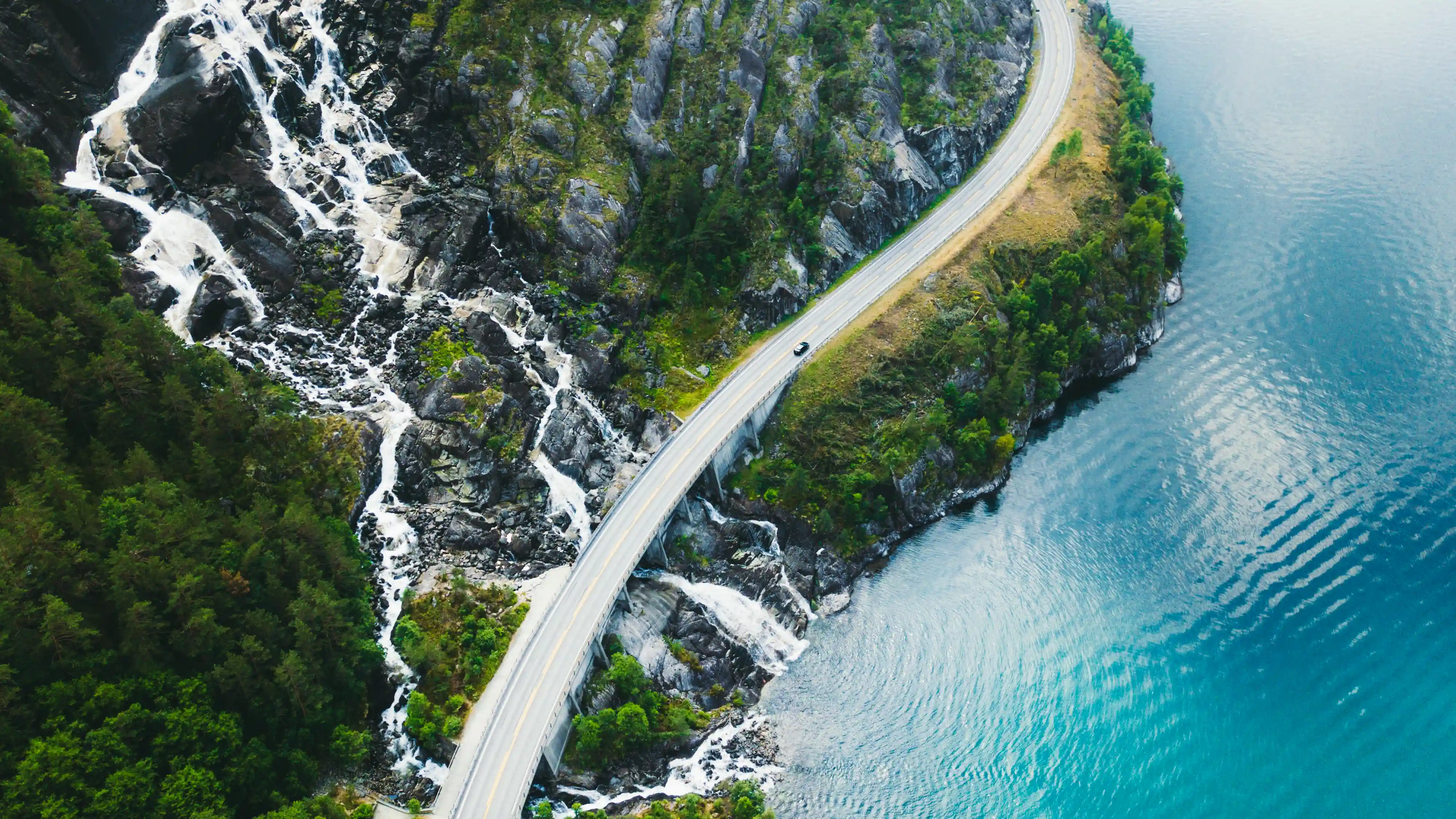 Aerial view of a truck driving along a winding coastal highway beside blue water, used on GIA Group, LLC’s Certificate of Insurance page to symbolize speed, reliability, and nationwide coverage.