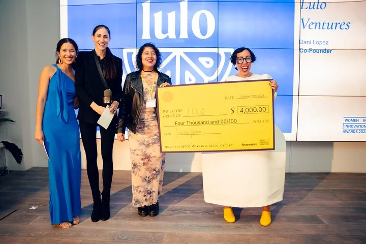 Four people stand together, smiling, holding a large novelty check at an event.