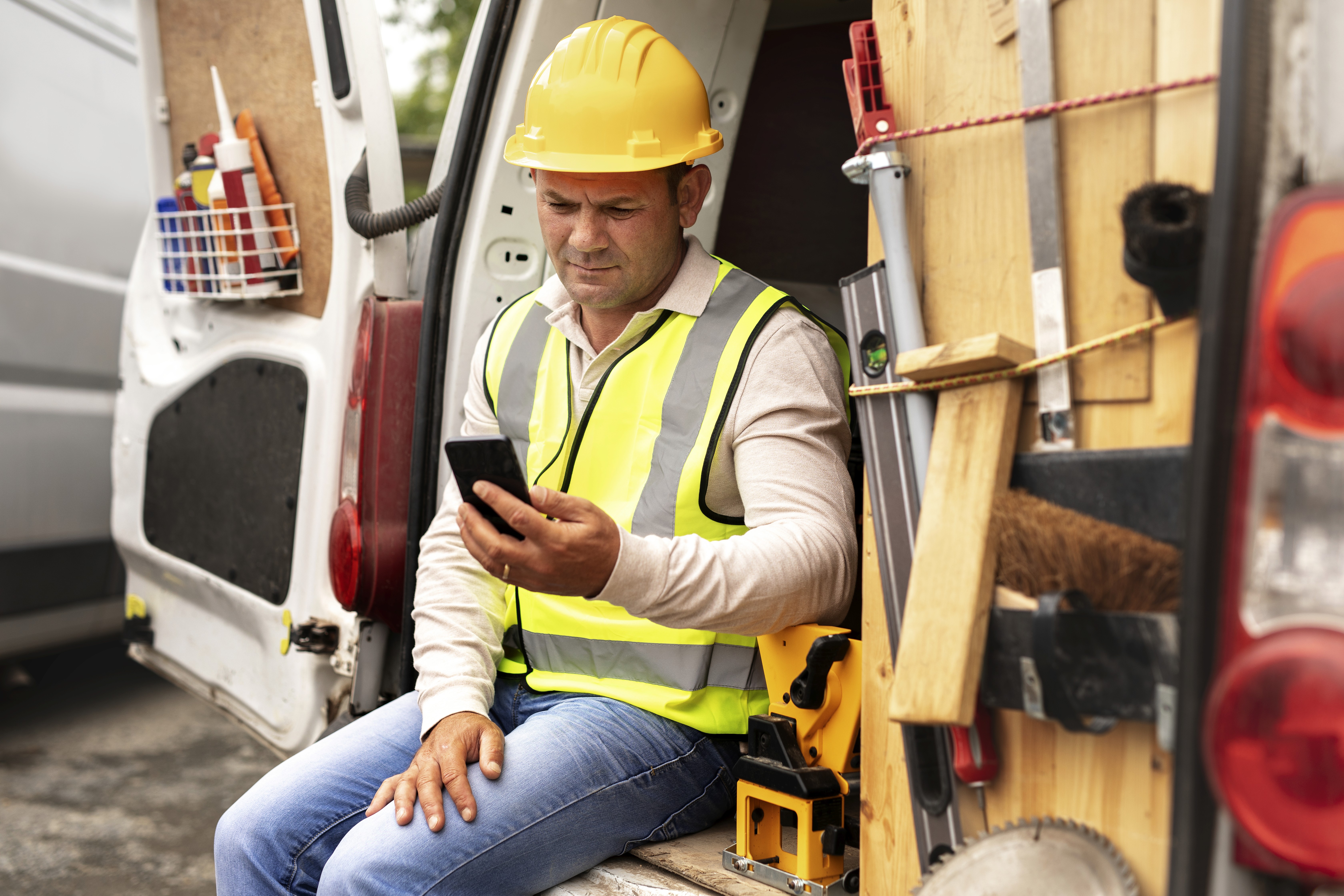 Tradesperson on a job site checking a customer message on their phone beside a work van