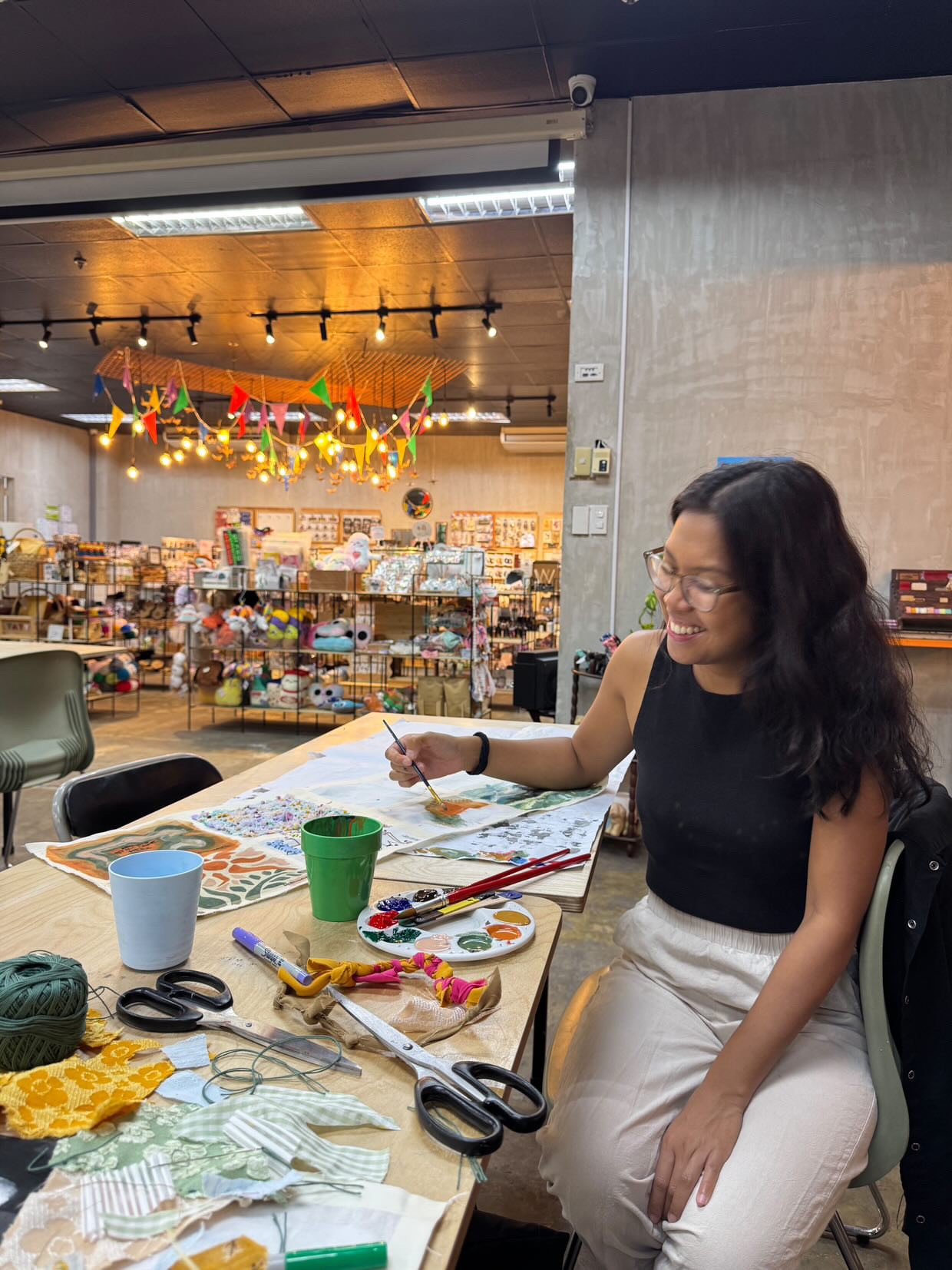 Una persona con una camiseta negra y pantalones de color claro está de pie en la cima rocosa de una montaña al atardecer, sosteniendo una cámara frente a su cara para tomar una foto. Un mar de nubes se extiende detrás de ellos, iluminado por la luz dorada del sol poniente.