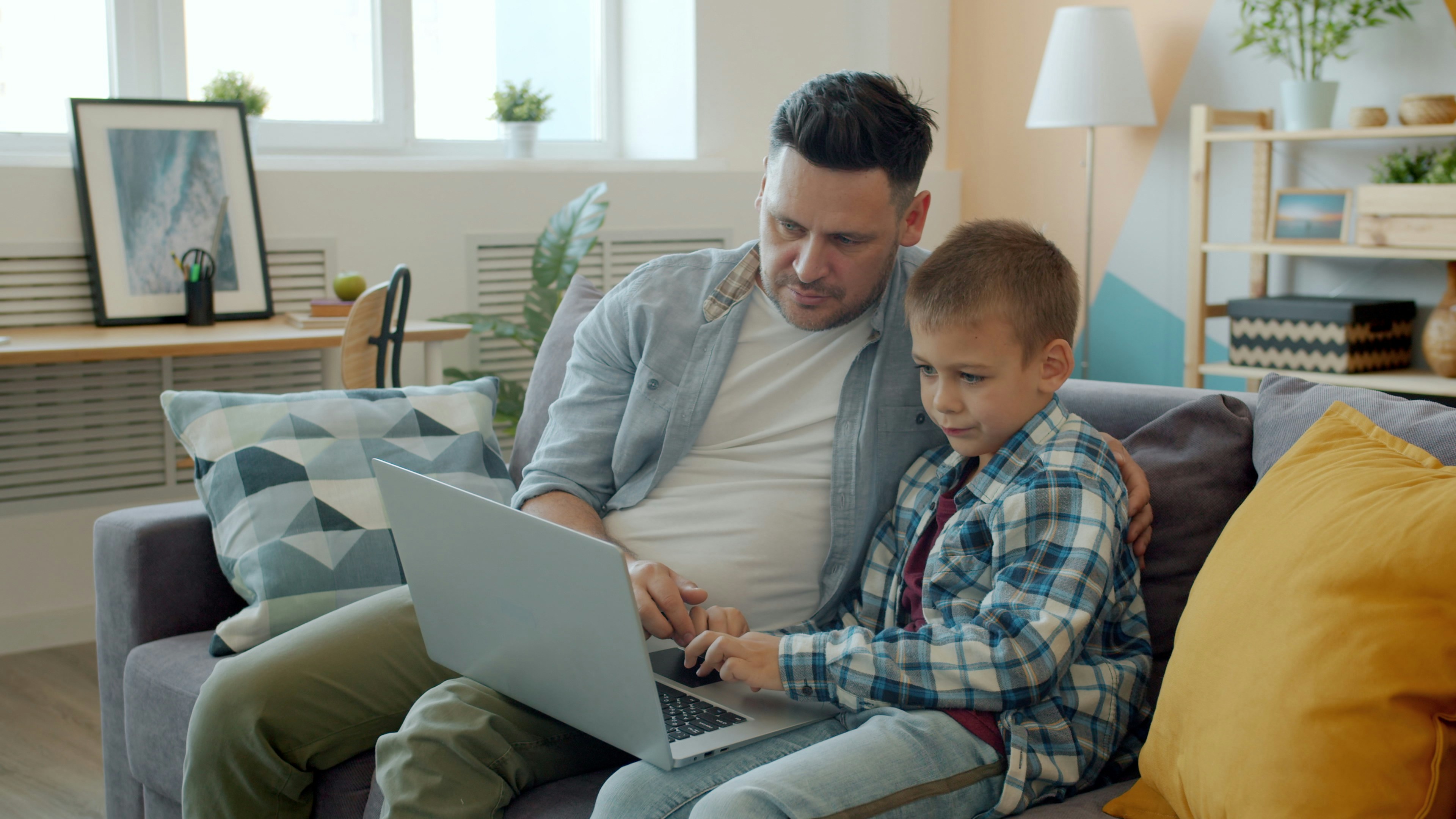 Father and son using a laptop on the couch.