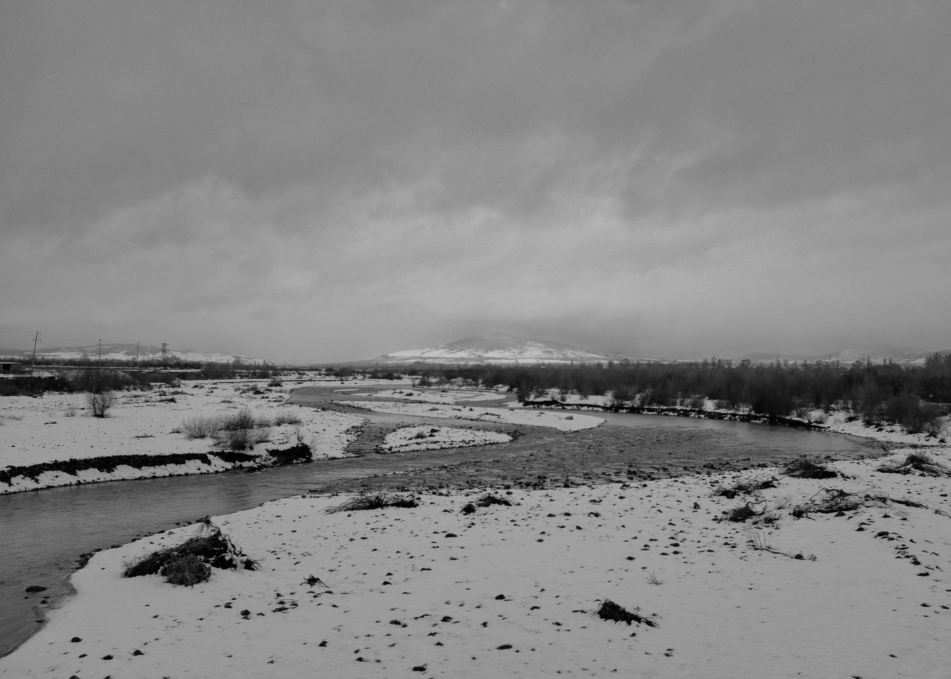 Snow-covered banks of a river curve through a wide valley beneath a cloudy sky. Power lines and distant hills mark the boundary of the occupied region.