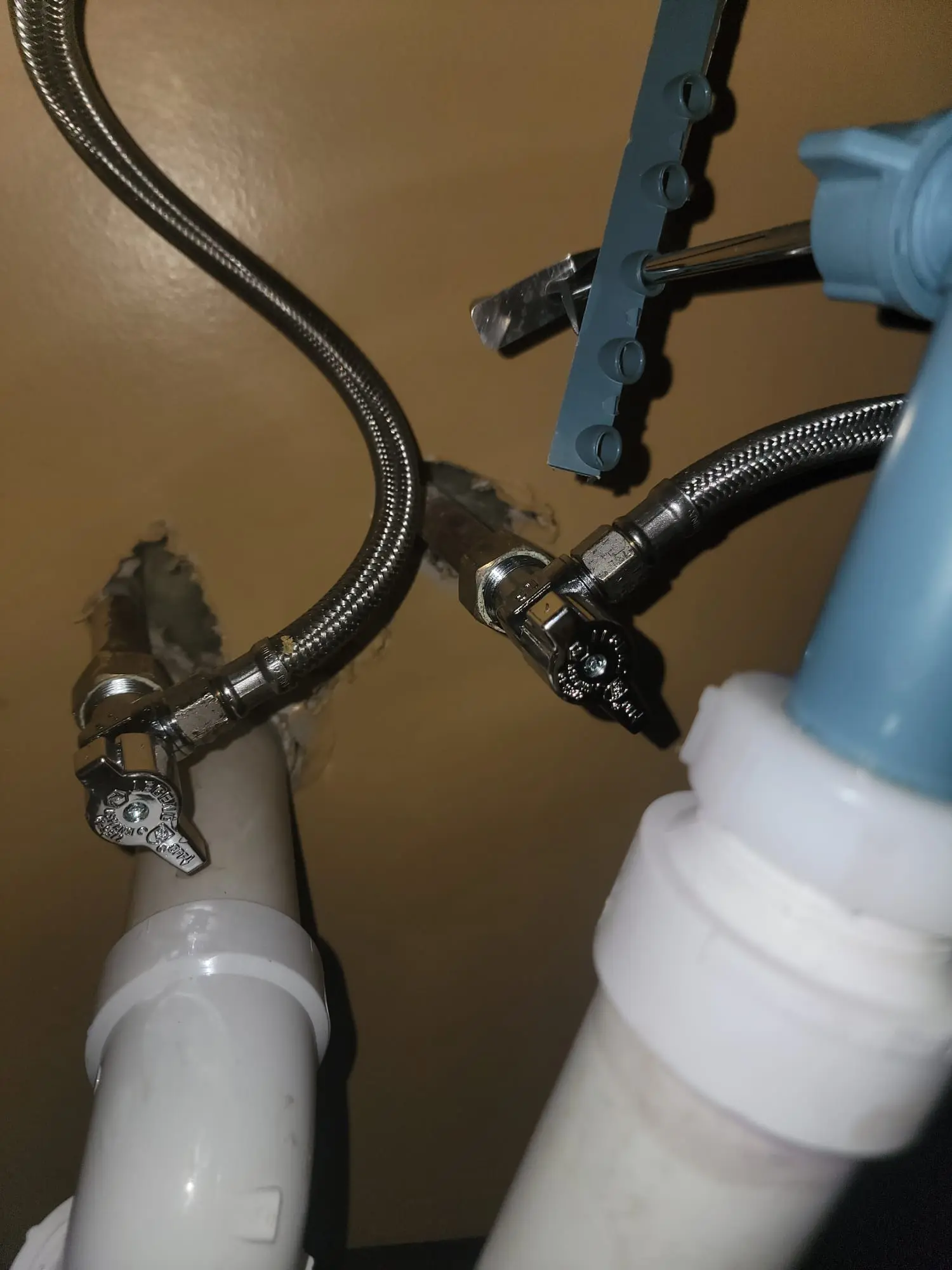 A close-up of under-sink water supply lines, shutoff valves, and PVC drain pipes inspected during a professional faucet and sink repair.