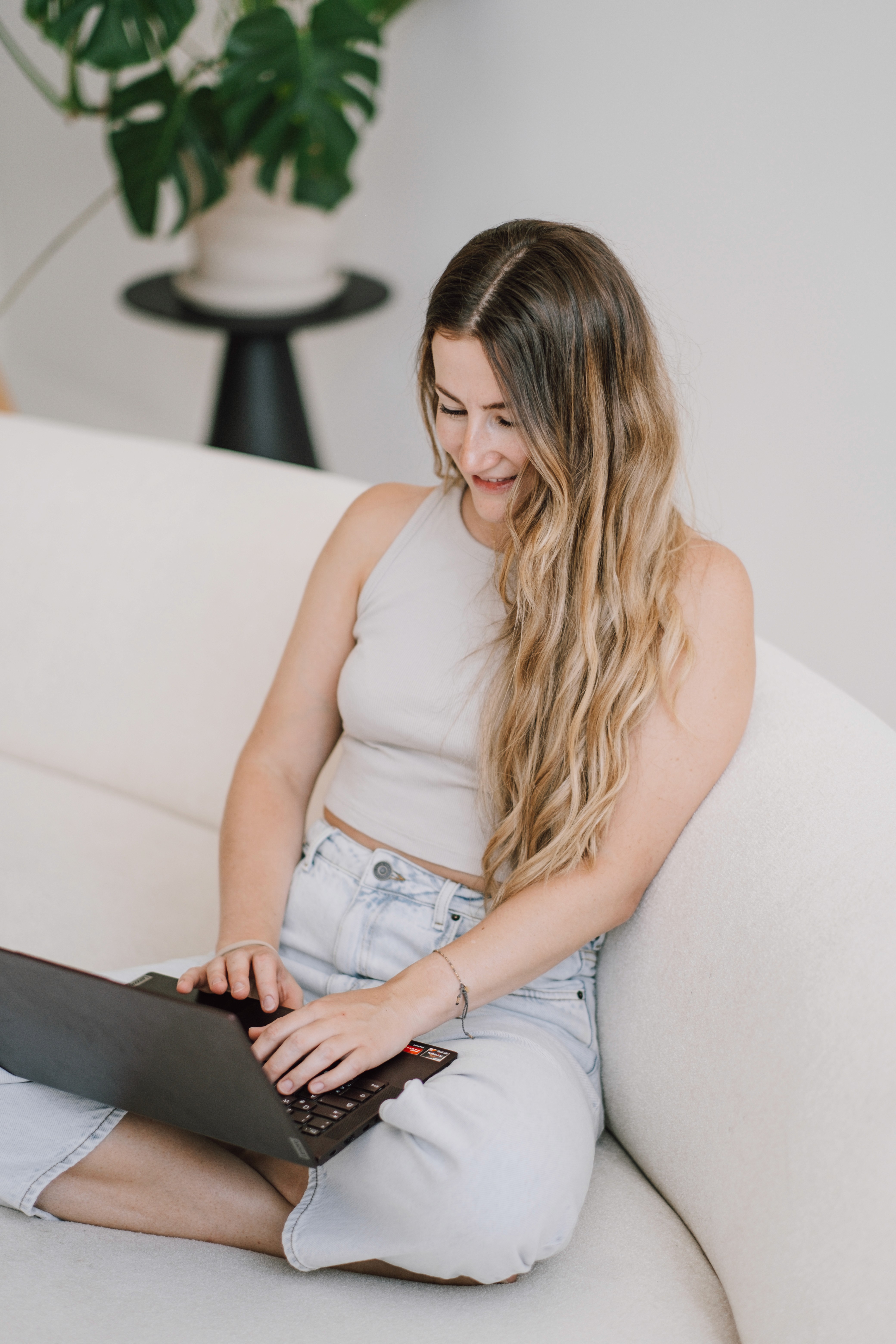 Antonia sitzt auf weißer Coach im Schneidersitz, mit dem Laptop auf dem Schoß