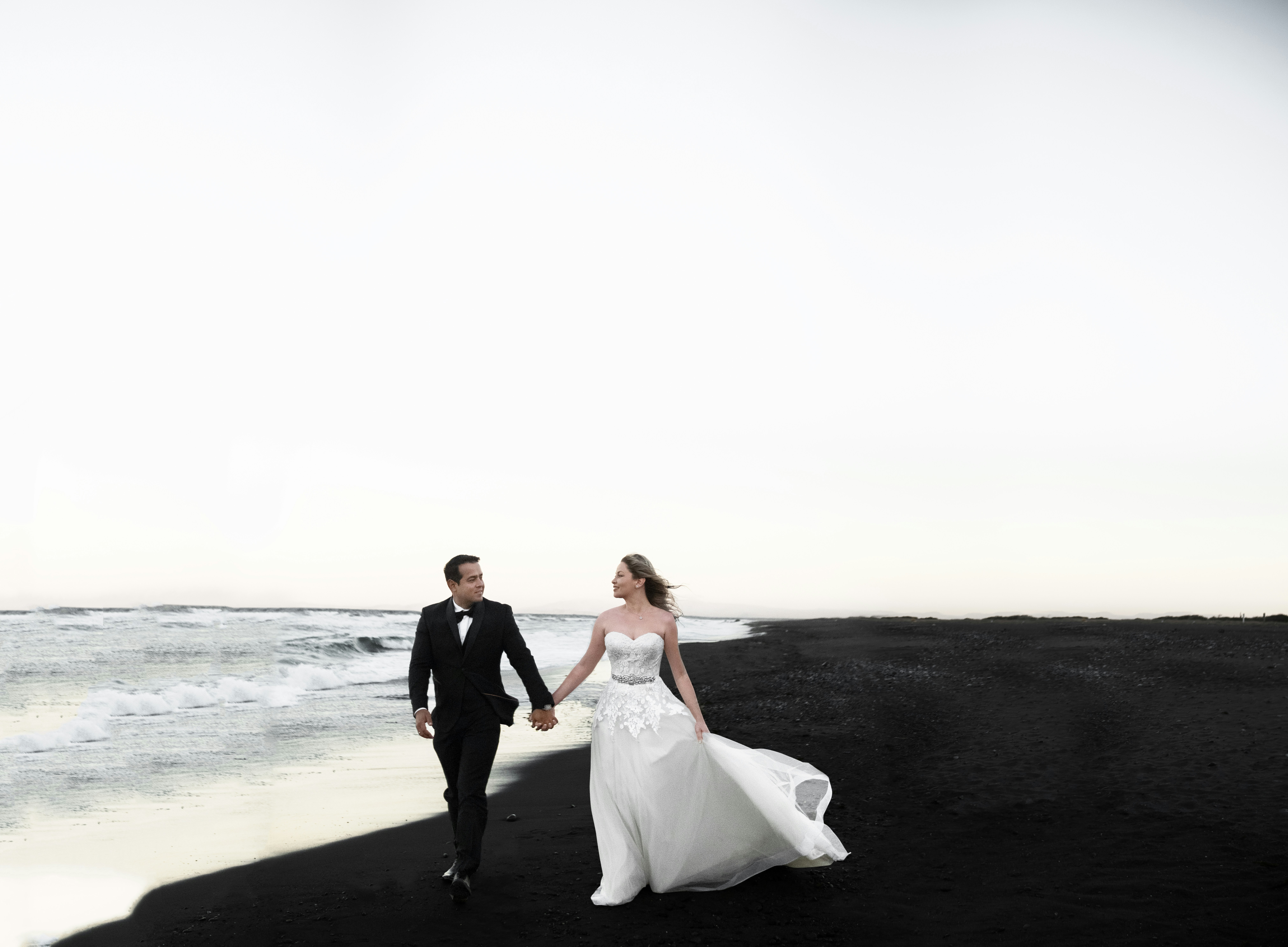 Bride and groom walking along a black sand beach in Iceland.