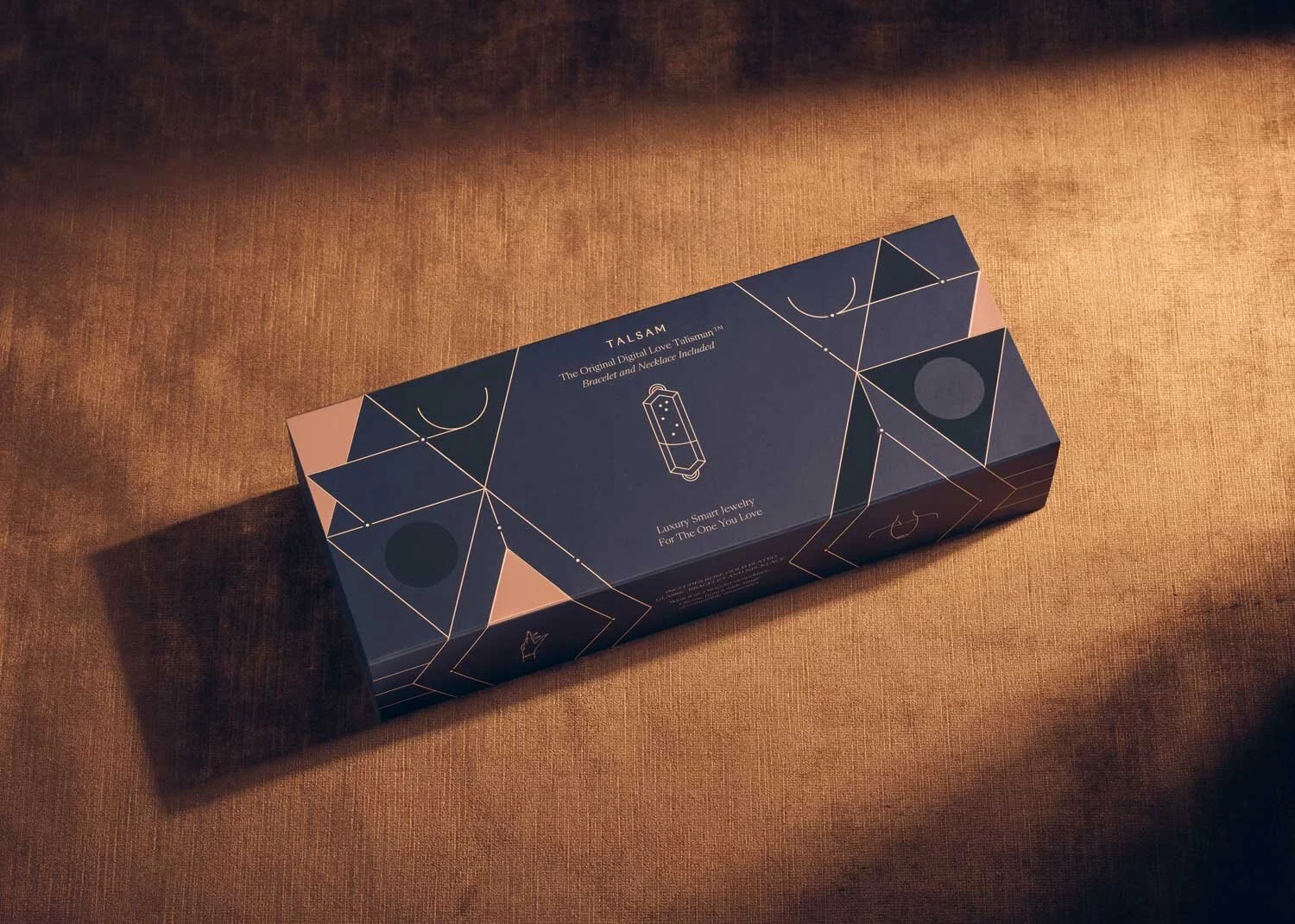 Closed Talsam smart jewelry packaging box with geometric gold linework on a warm metallic surface