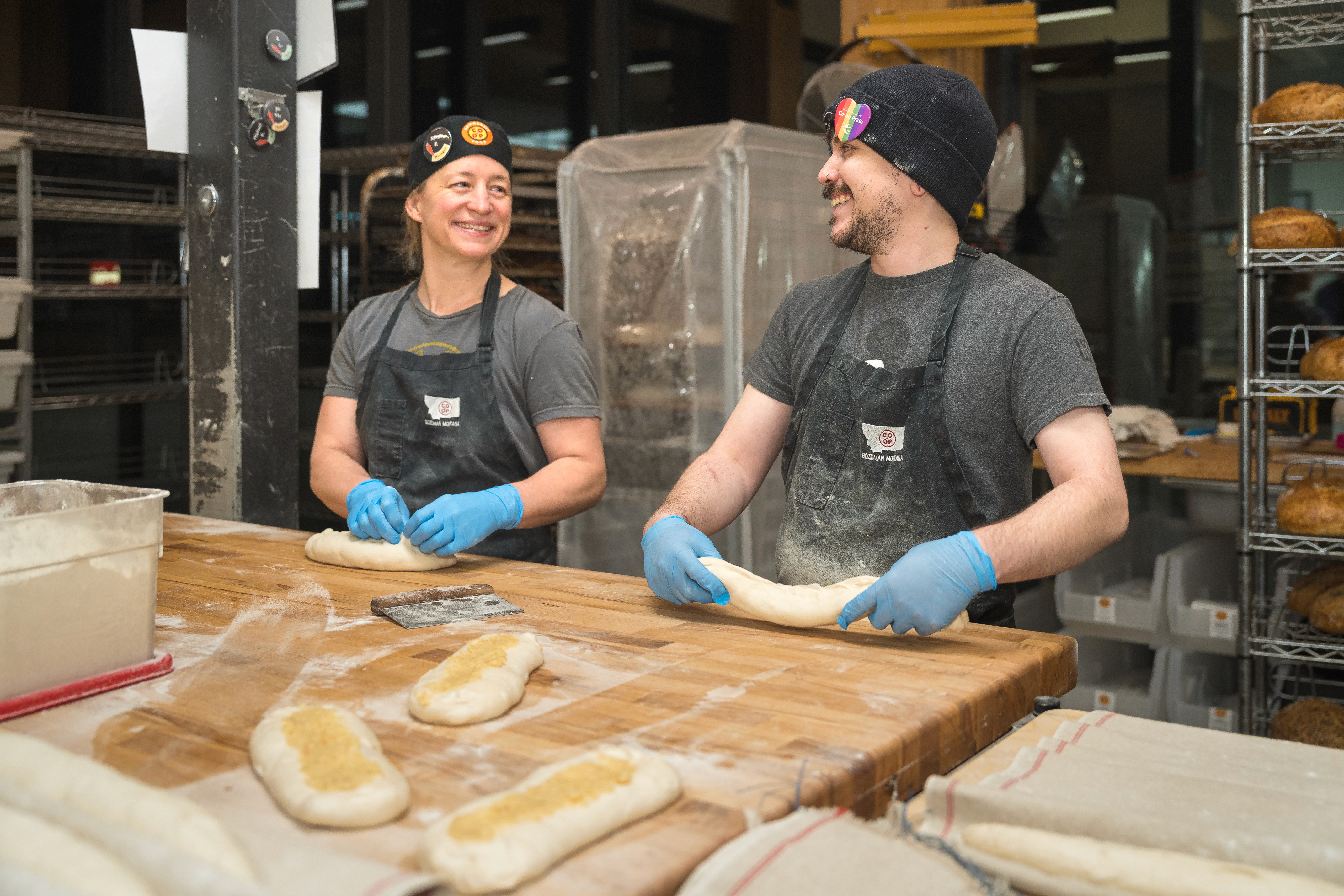 A smiling person stands in front of a display case filled with baked goods, showcasing a variety of items.