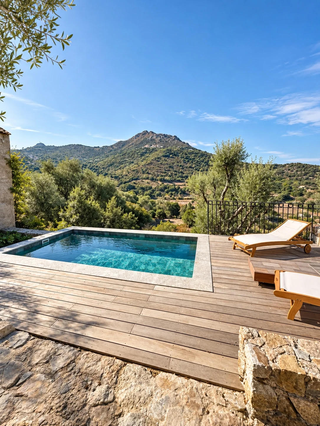 Piscine avec terrasse en bois et transats devant un paysage de collines méditerranéennes.