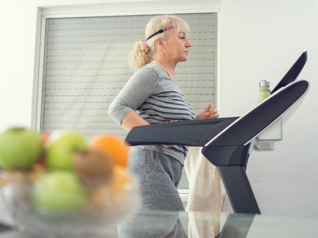 senior woman walking on a treadmill to complement her seated fat-burning workout plan
