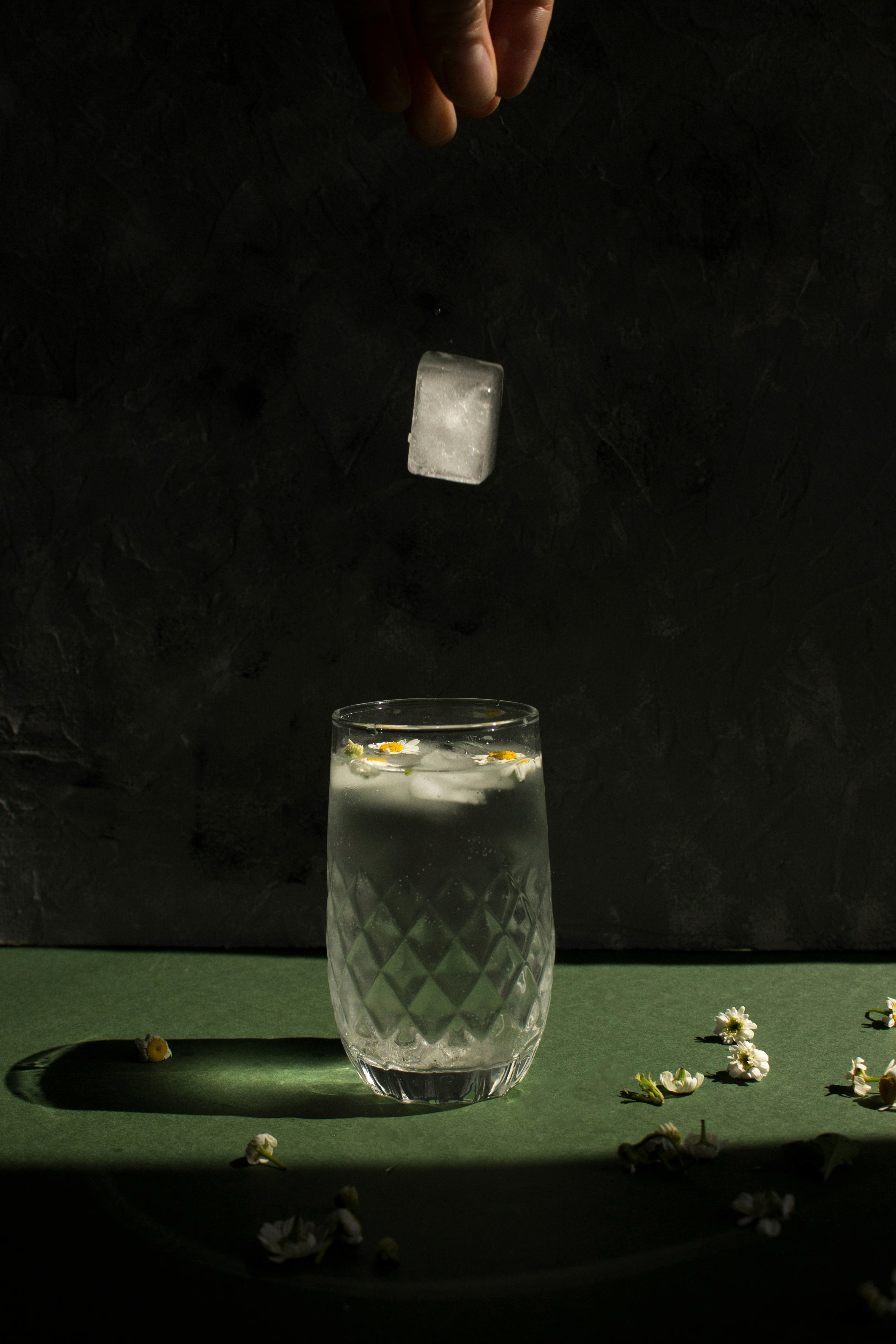 a glass of water with a flower into which an ice cube falls