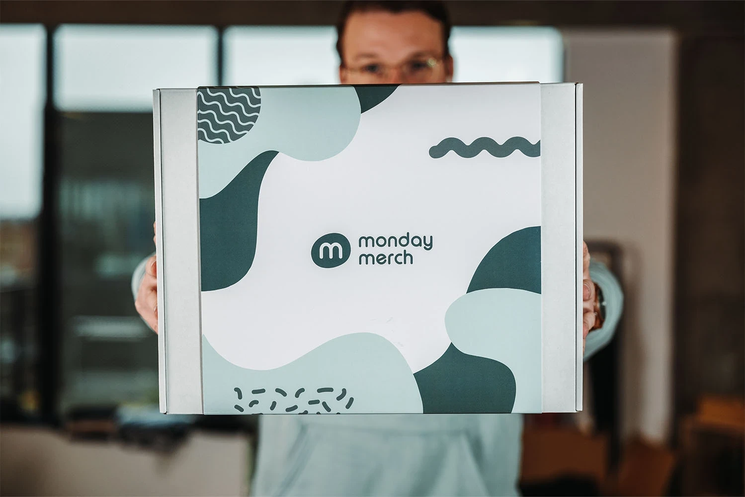 A person holding a box with the "monday merch" logo and abstract shapes