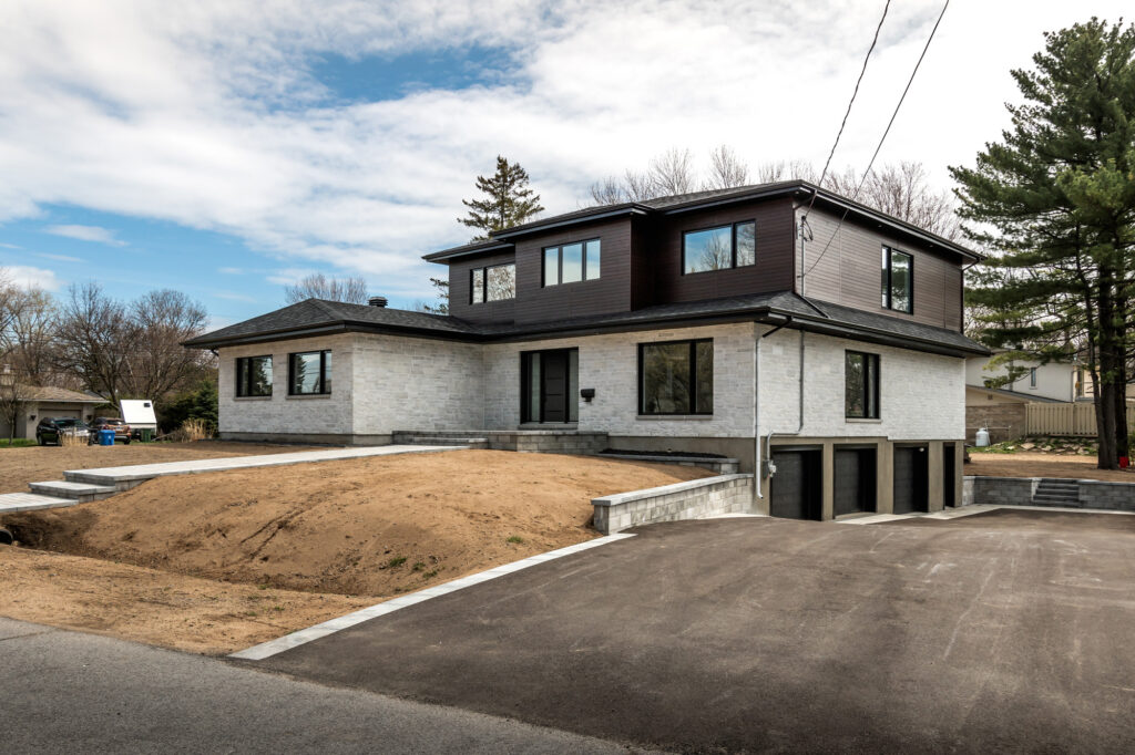 Modern two‑storey home with dark upper and light stone‑clad lower exterior, paved front walkway and large windows showcasing the high‑end residential properties serviced by B&Y Reno Corp