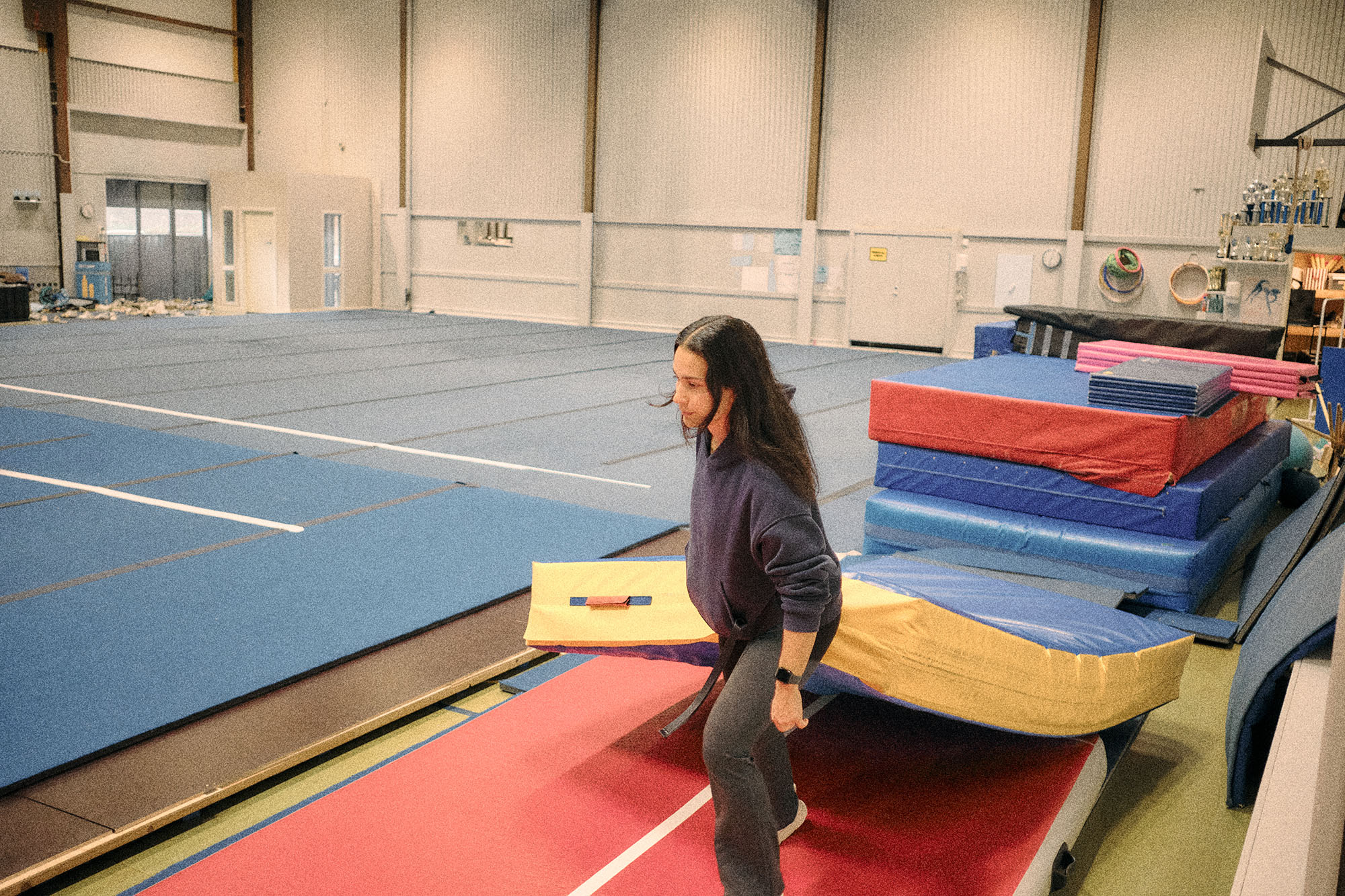 Två personer som gör kullerbyttor på en löparbana med skog och en papperskorg i bakgrunden.