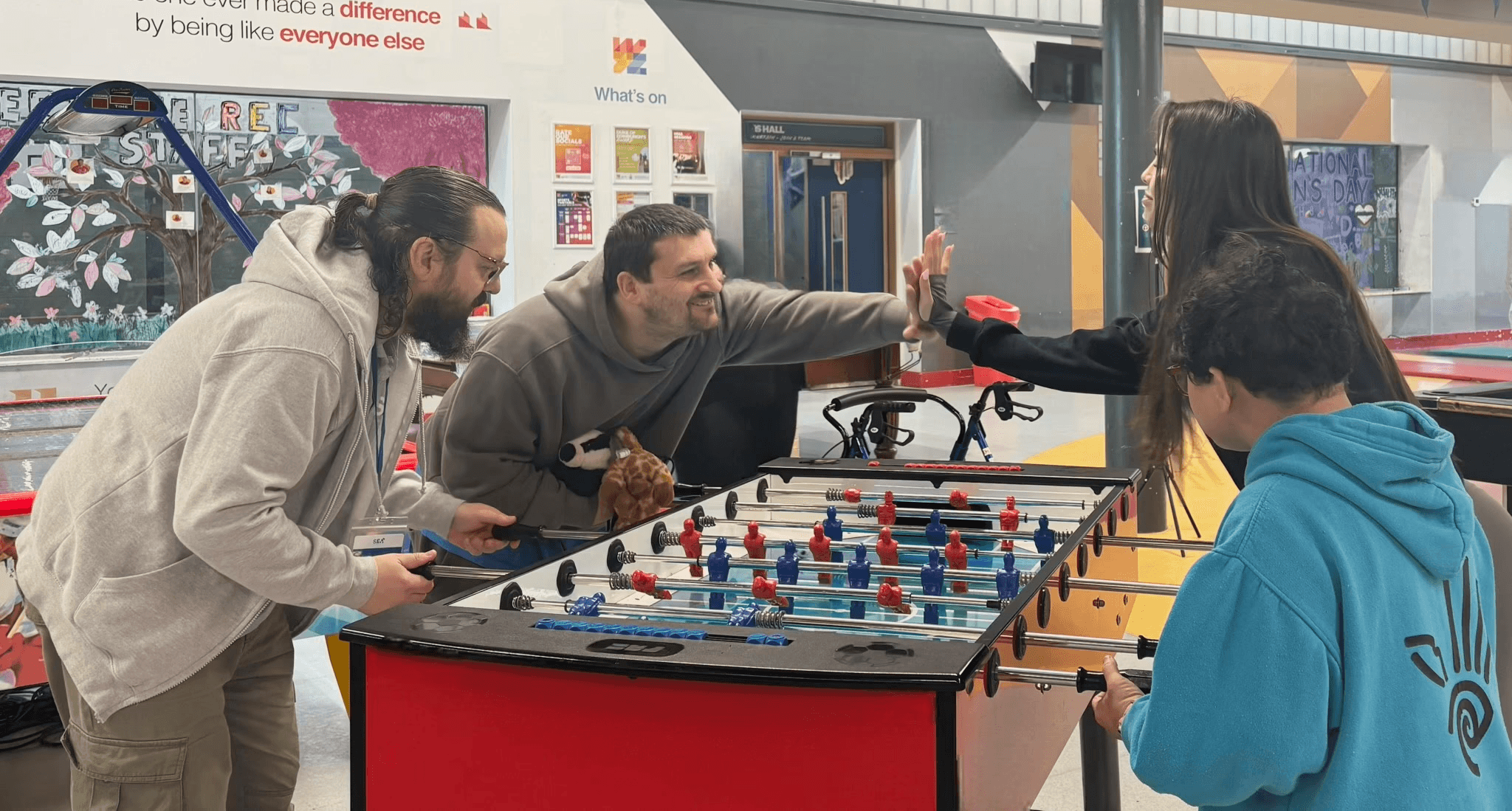 A group of people with disabilities playing table football together in a community activity room