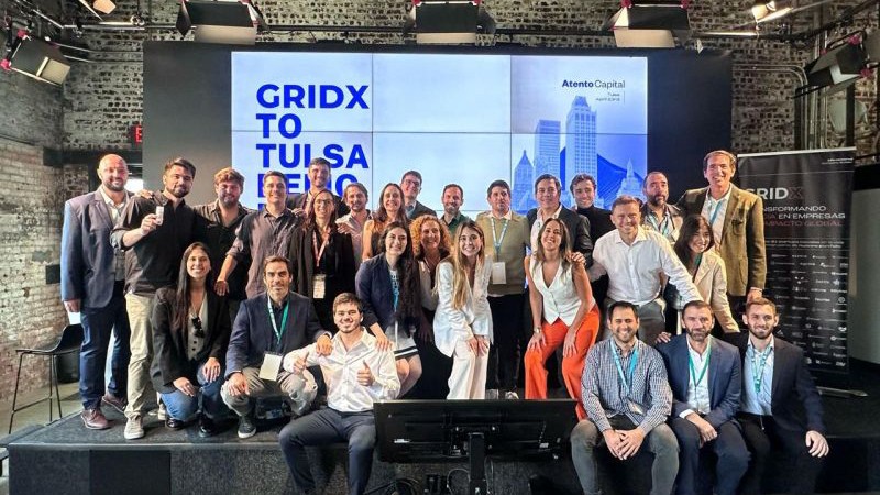 A diverse group of people poses smiling on the stage of the event "GridX to Tulsa Demo".