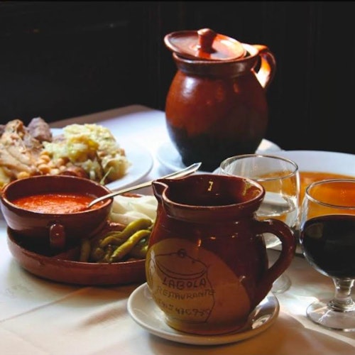 擺滿陶瓷壺、食物碗、兩杯葡萄酒、烤肉和蔬菜的餐桌。