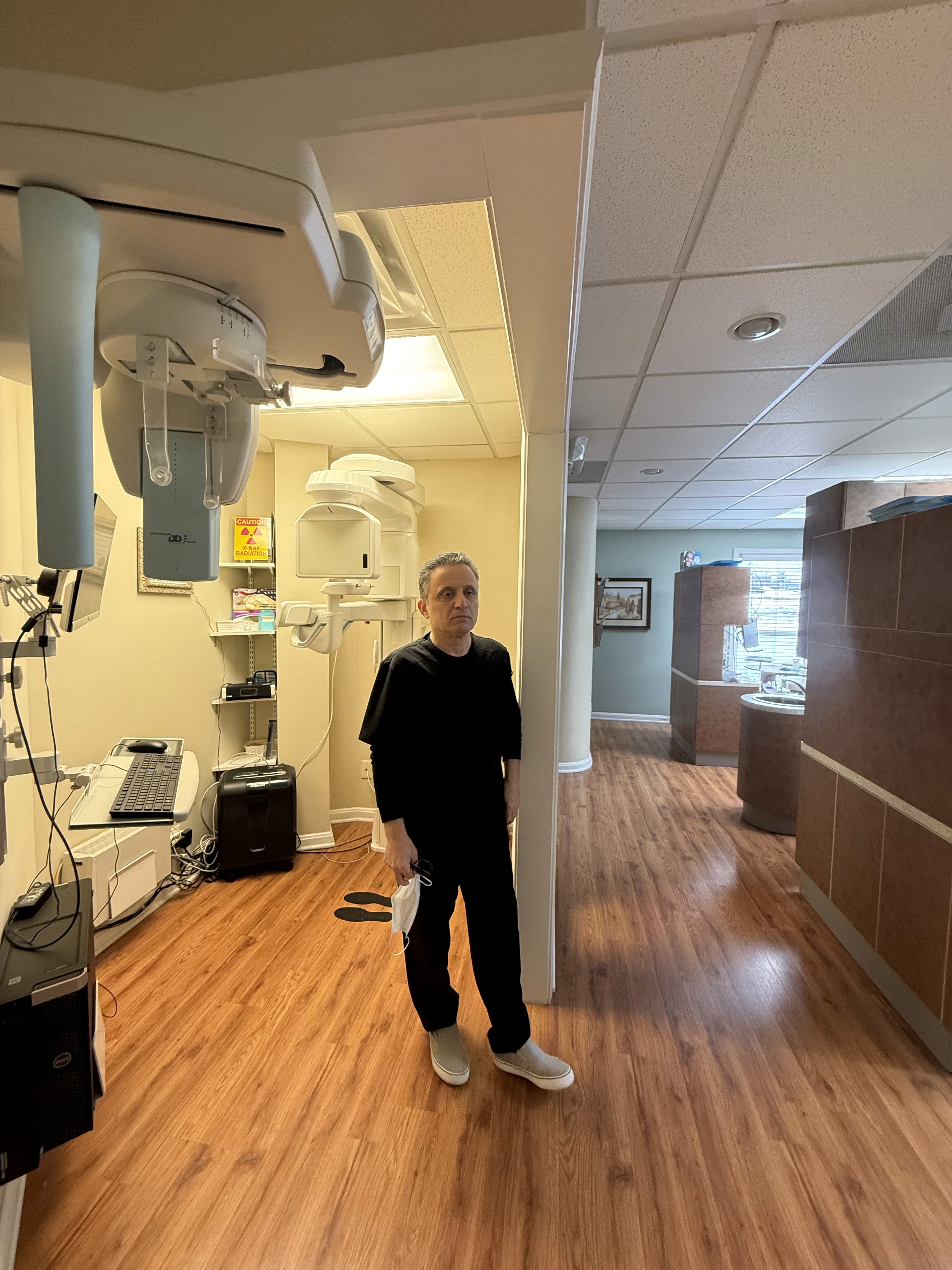 Dentist stands in exam room, wearing scrubs, holding a mask.