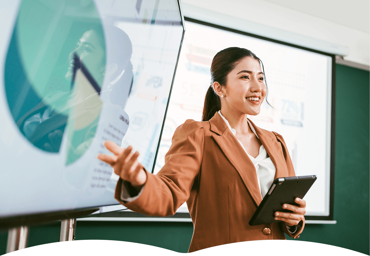 A business professional gives a presentation in an office setting, utilizing a digital tablet and a large screen displaying charts and data visualizations, highlighting concepts of workplace collaboration and technology integration.