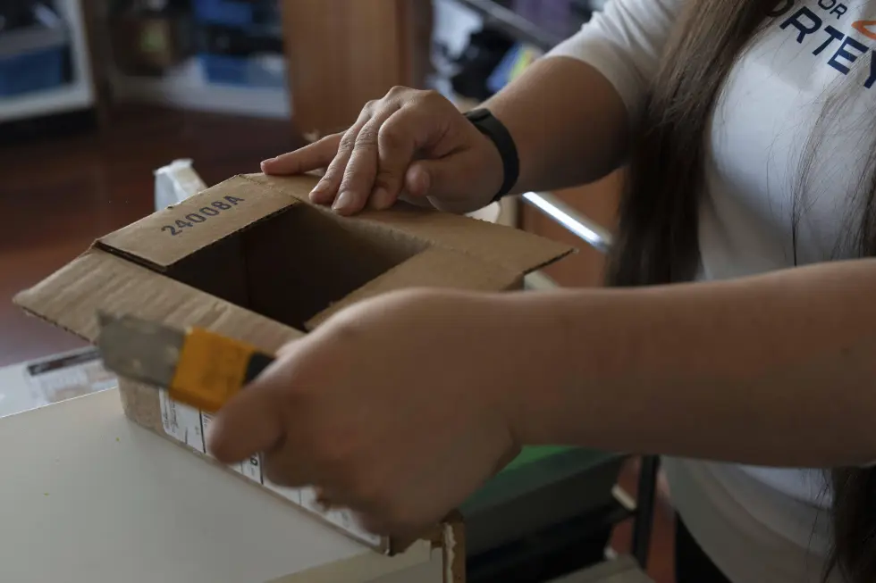 Amanda Follett opens packages at A Sight For Sport Eyes, a brick-and-mortar and e-commerce store for sport goggles, Aug. 20, 2025, in West Linn, Ore. (AP Photo/Jenny Kane)