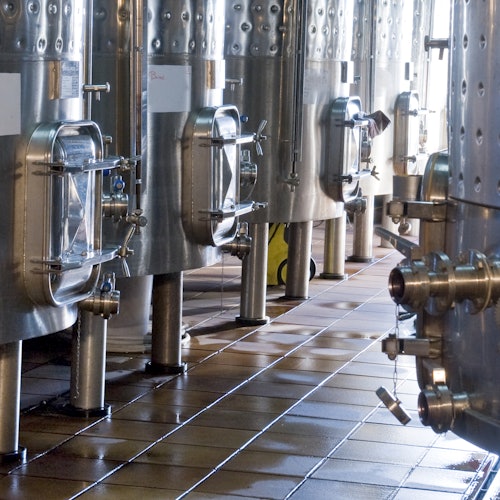 Large stainless steel tanks with glass hatches and valves on a tiled floor, likely in a brewery or industrial facility.